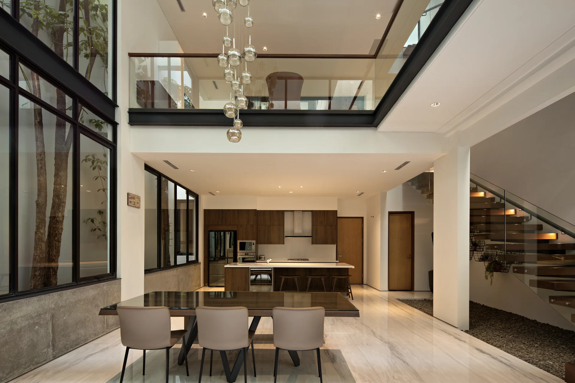 A modern open-plan dining room with a double-height ceiling, a cascading glass globe pendant light, and a floating staircase.