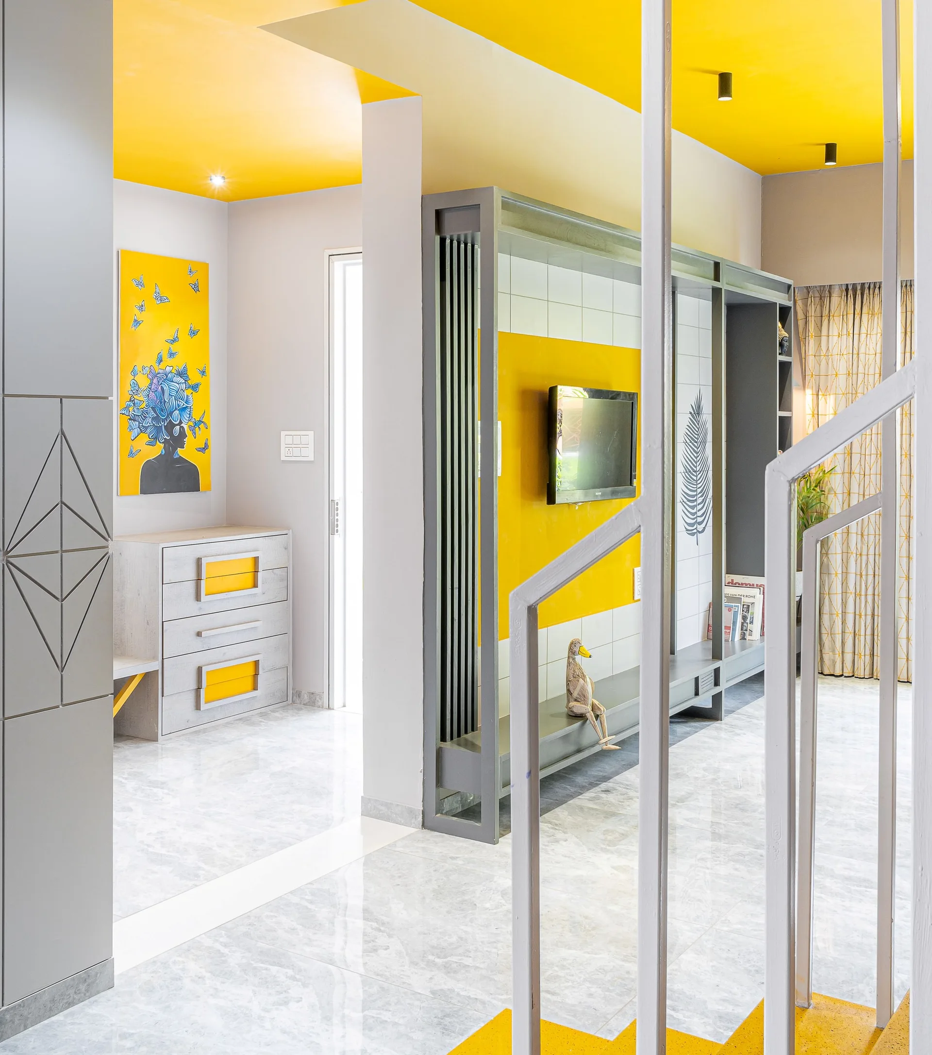 A modern hallway and living area with a bright yellow ceiling, light grey marble floors, and grey built-in cabinets with yellow accents.