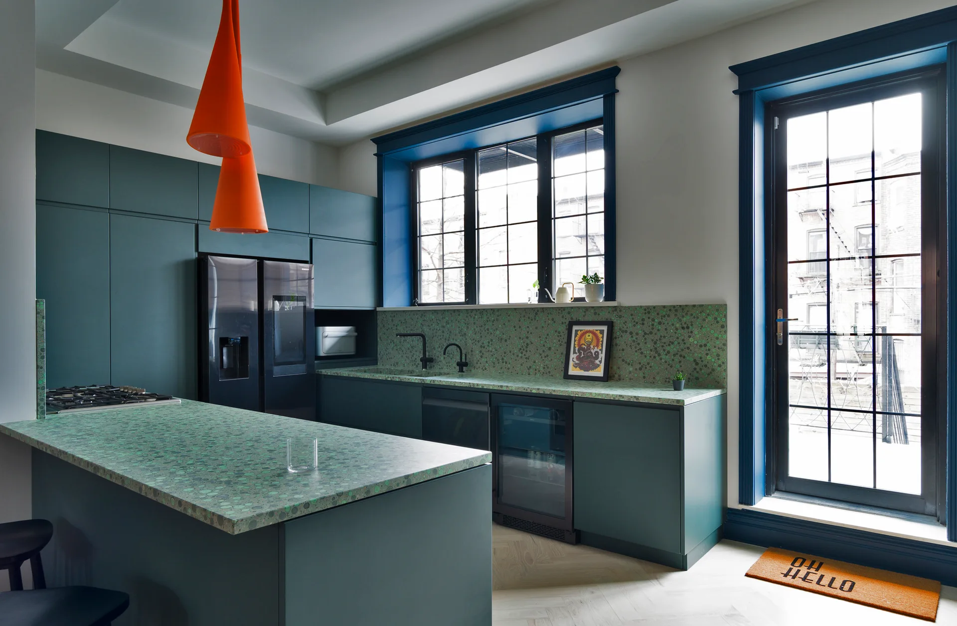 Modern kitchen featuring teal cabinetry, green speckled countertops, black appliances, and two orange cone pendant lights.