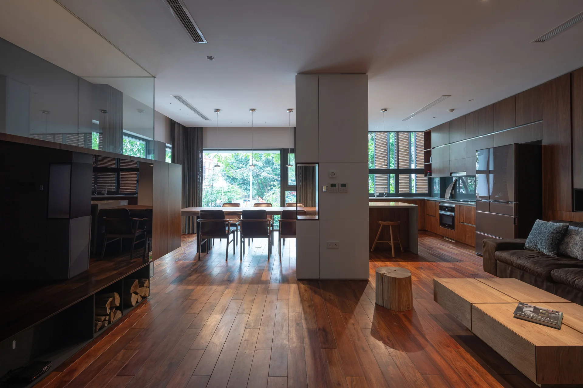 A modern open-concept living area with dark wood flooring, extensive wood cabinetry, dining table set, and a central white partition pillar.
