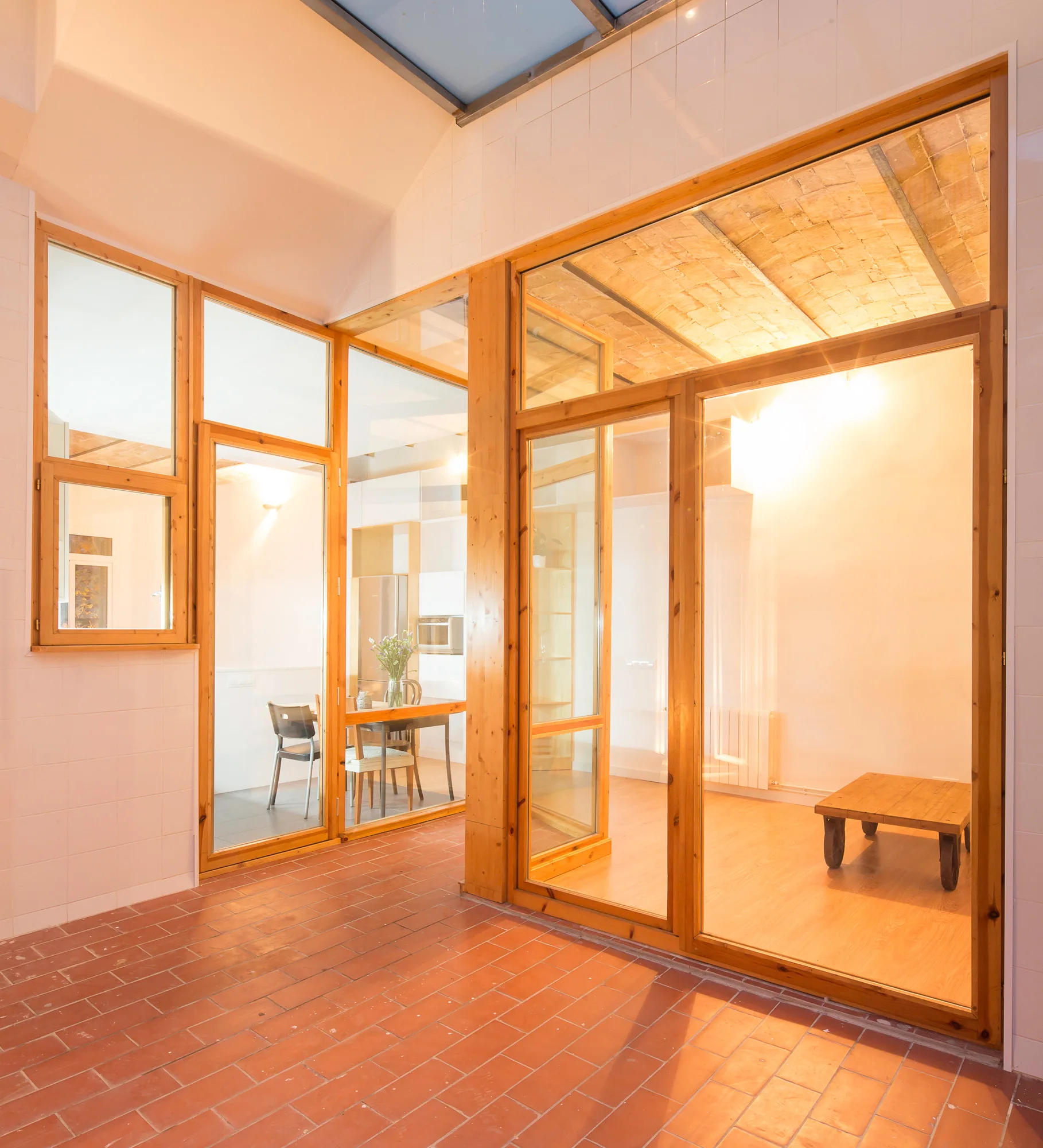 An indoor space featuring terracotta tile floors, wood-framed glass wall dividers, and an exposed brick vaulted ceiling.