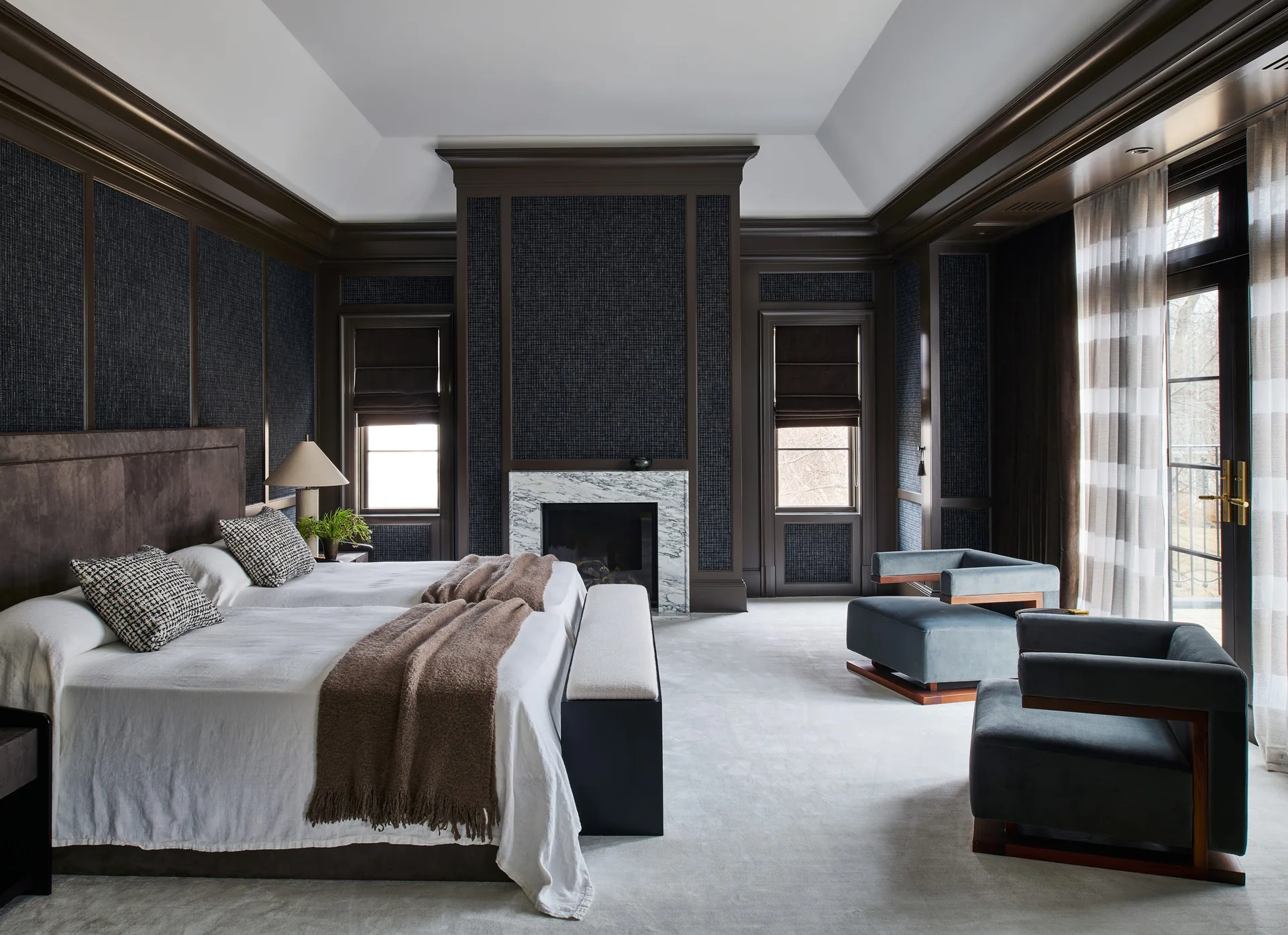 A bedroom featuring dark textured wall panels, two twin beds, and a white marble fireplace flanked by windows.