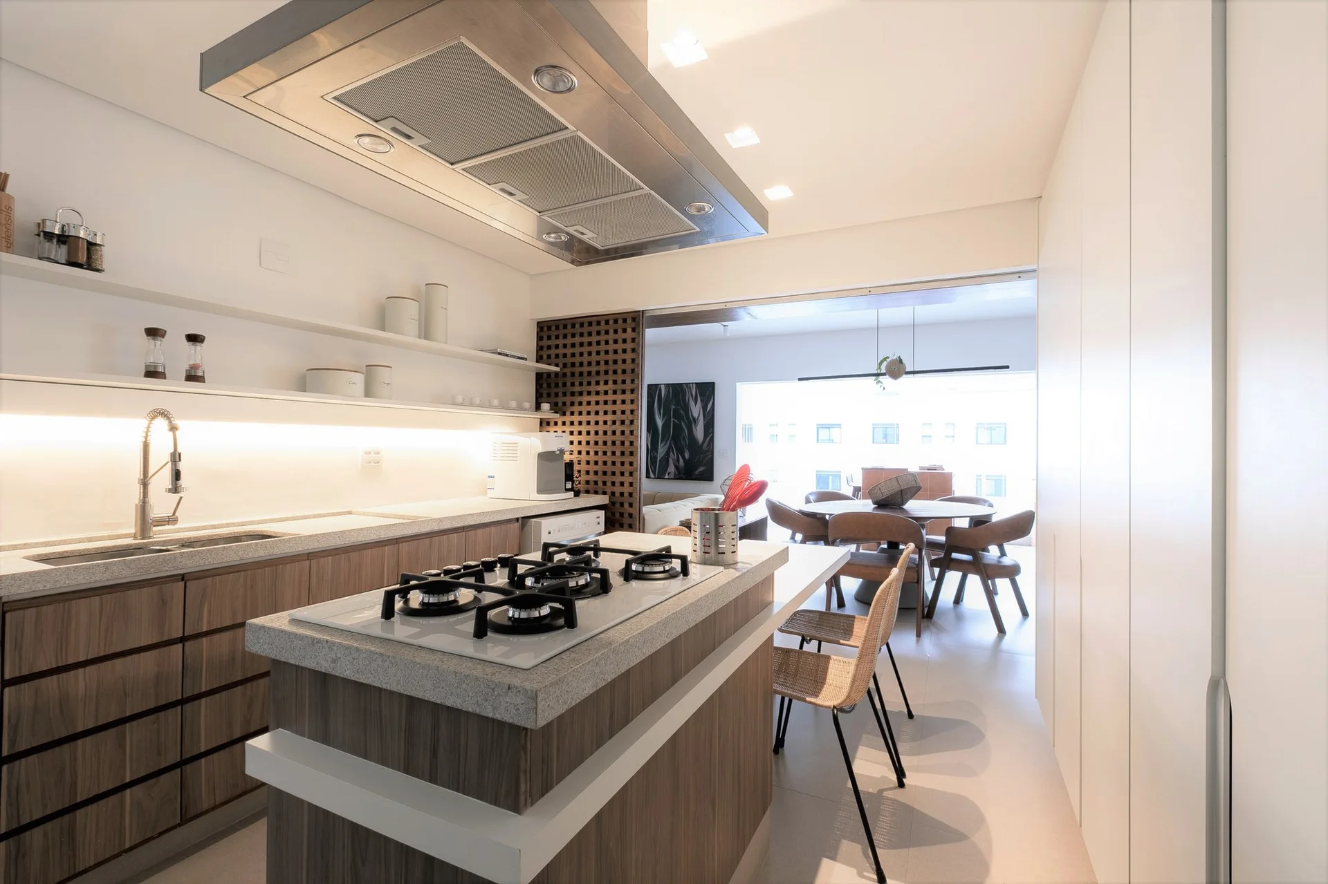 A modern kitchen featuring a wood-toned island with a cooktop, floating shelves with under-cabinet lighting, and a wooden lattice room divider.