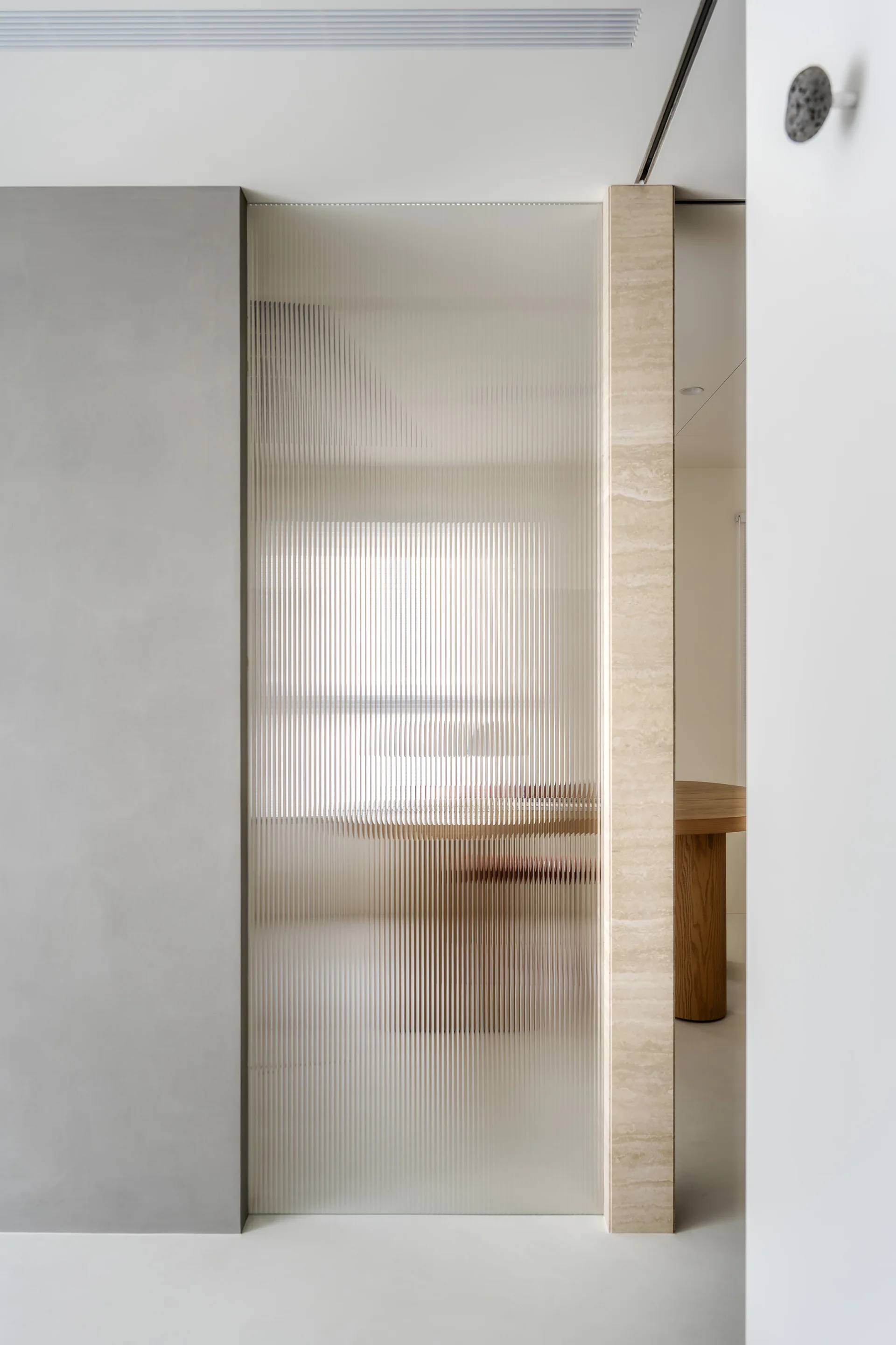 A minimalist interior detail featuring a ribbed glass partition set between a smooth grey wall and a beige stone column.