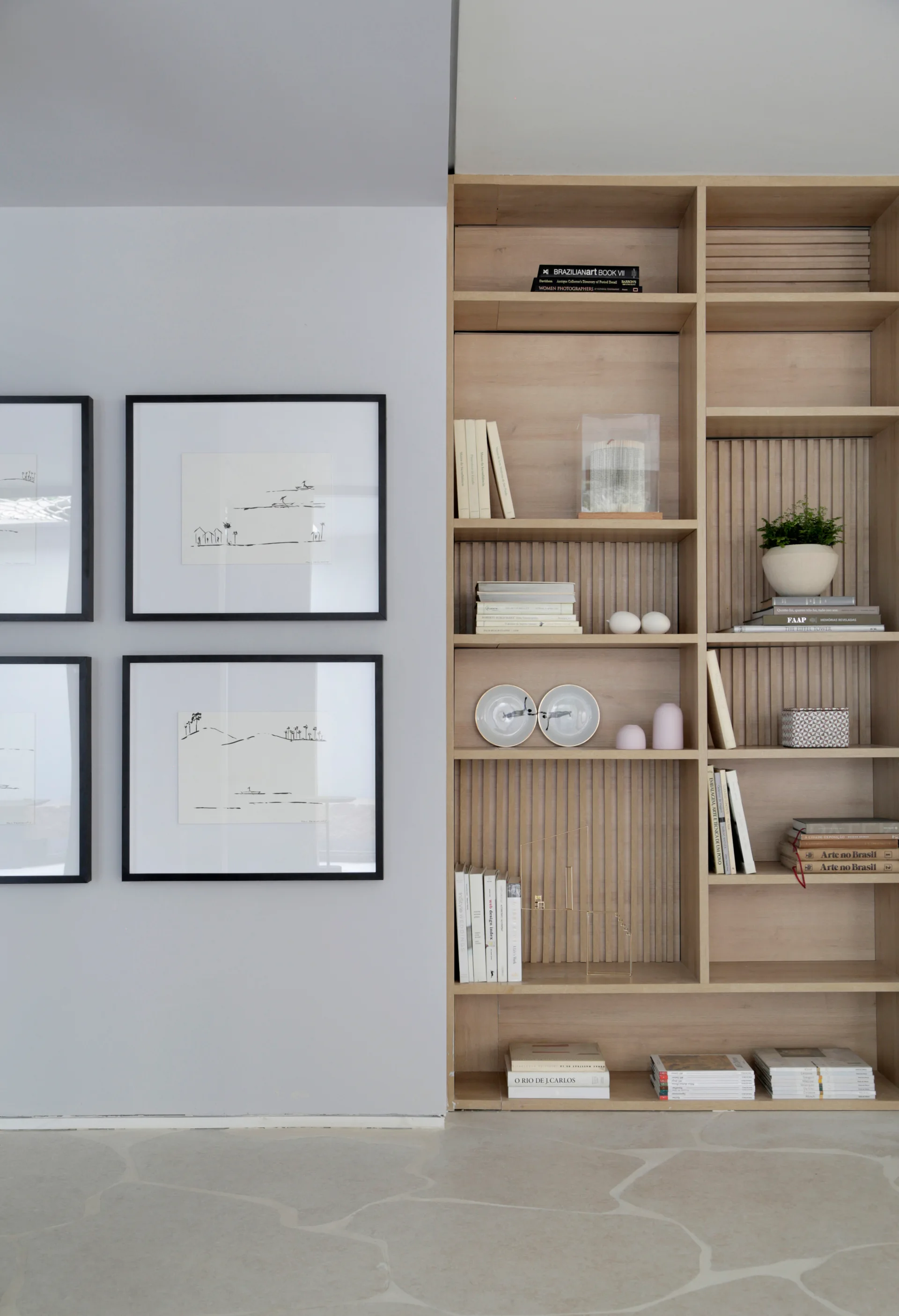 A light wood built-in bookshelf with slatted backing sits next to a light grey wall with four black-framed line art drawings.