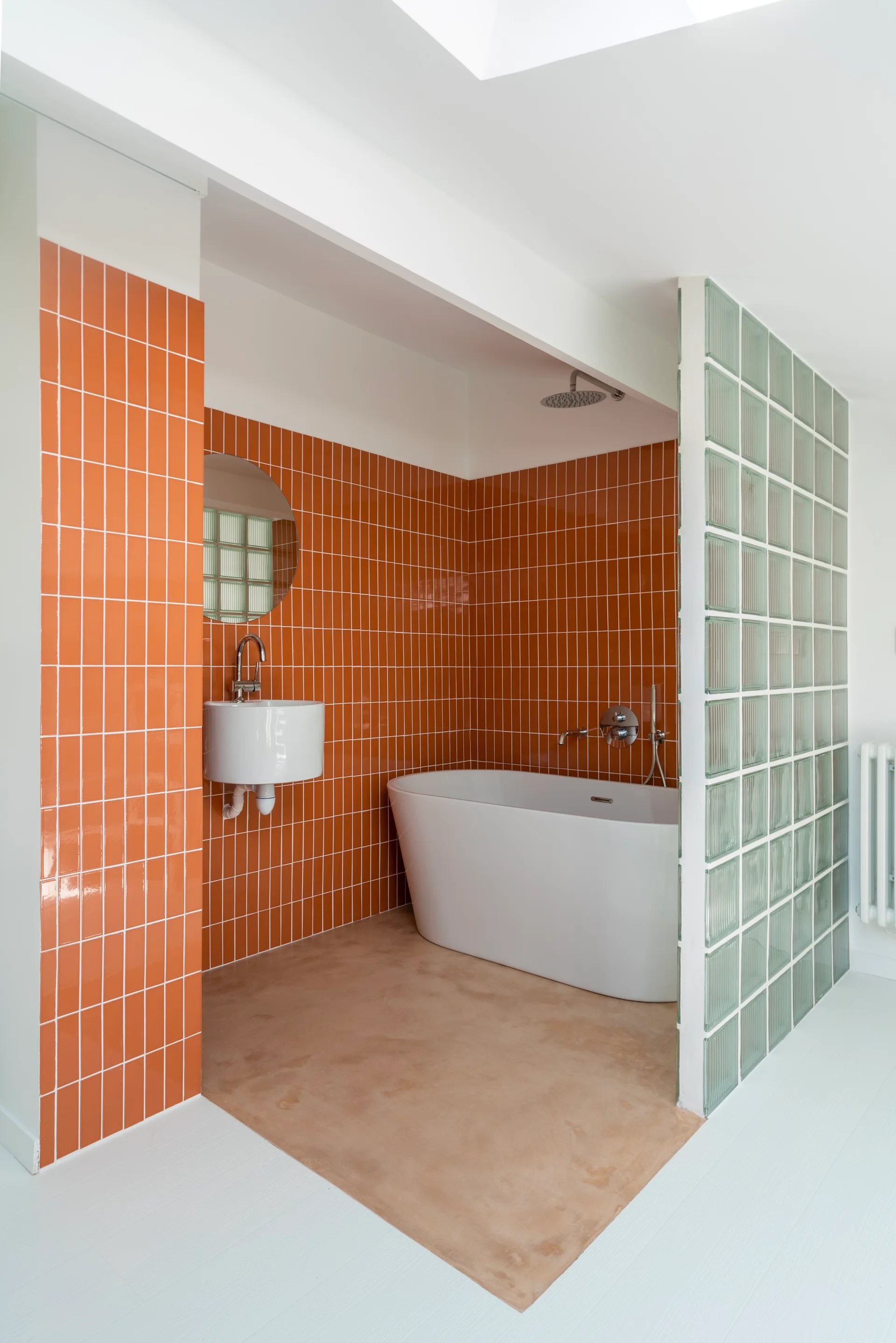 A modern bathroom features orange grid-tiled walls, a white freestanding bathtub, and a translucent glass block partition.