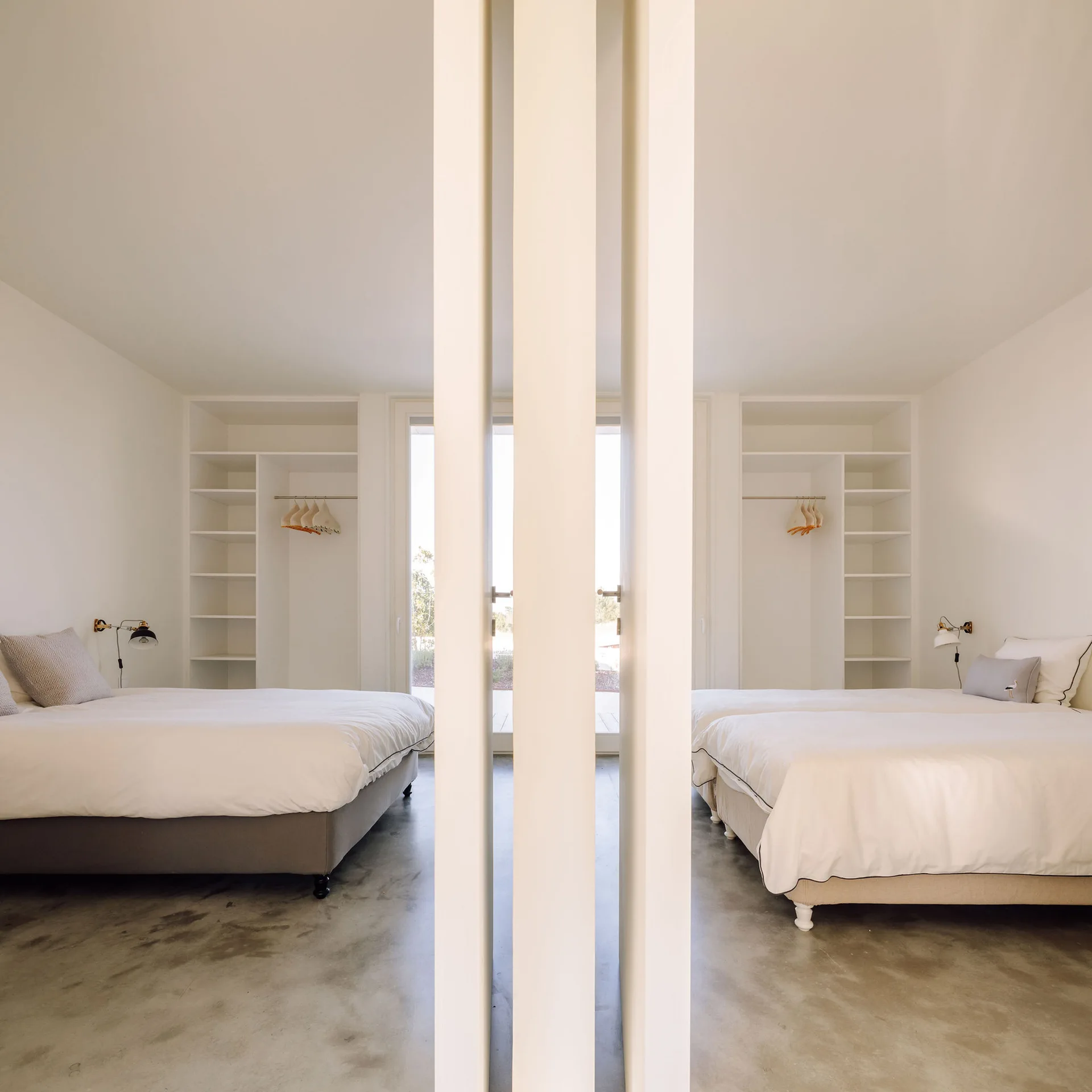 A symmetrical view of two identical beds with white linens and built-in wardrobes on either side of a central white partition.