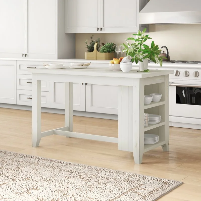 A white wooden kitchen island with open side shelves displaying ceramic bowls rests on a light wood floor next to a patterned rug.