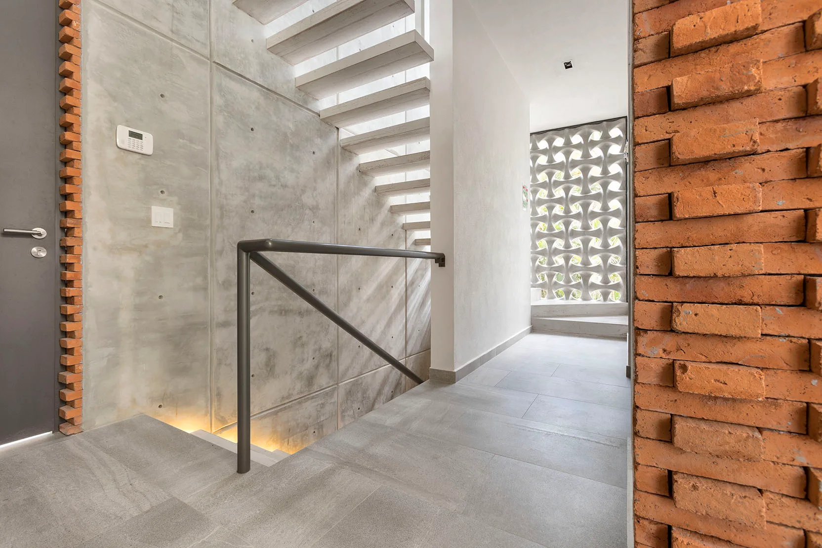 A modern interior staircase hallway featuring board-formed concrete walls, floating steps, and a decorative white breeze block screen.