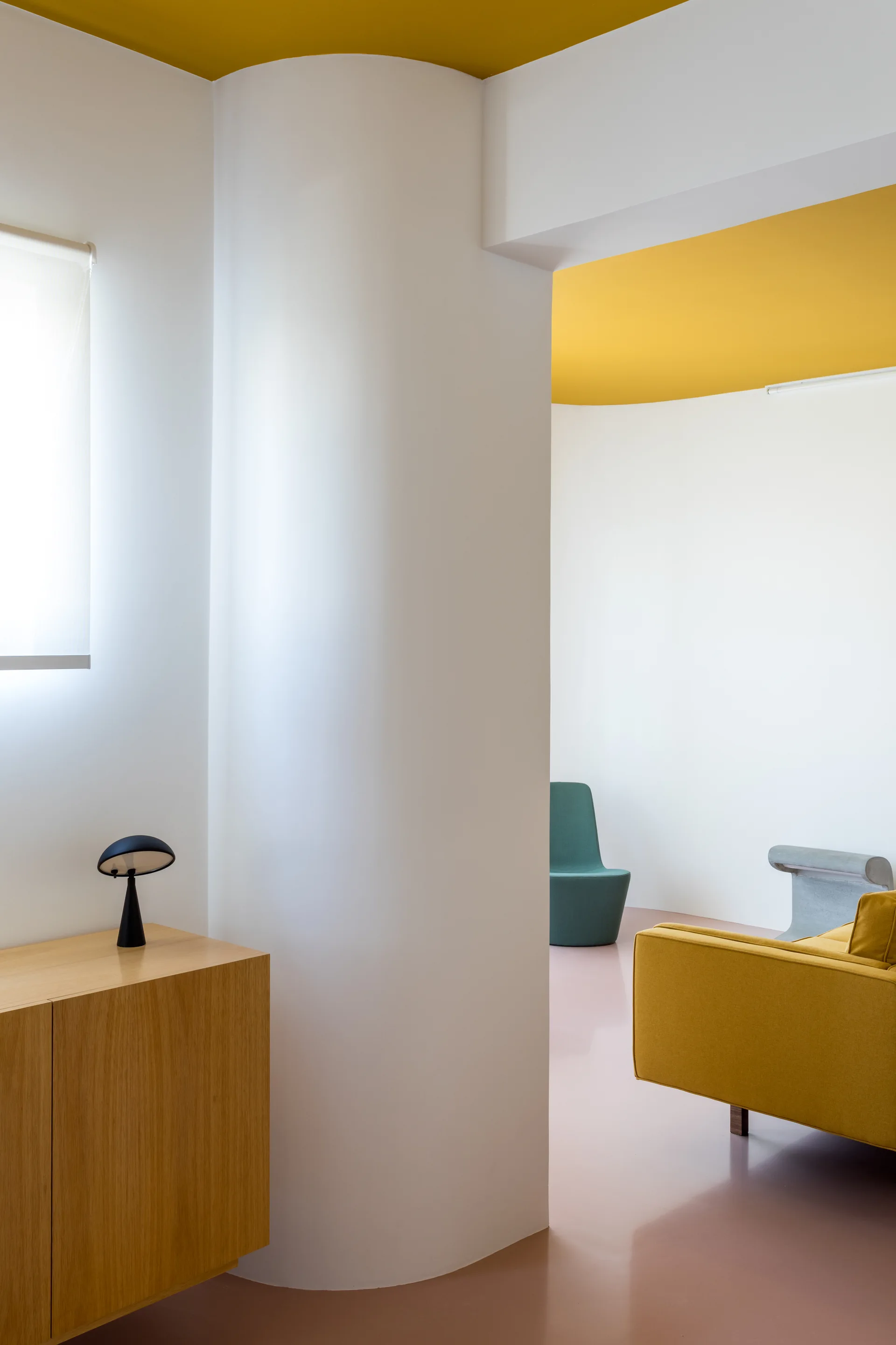 A modern room featuring a white curved column, a painted yellow ceiling, a pink floor, and a wood sideboard with a small black lamp.