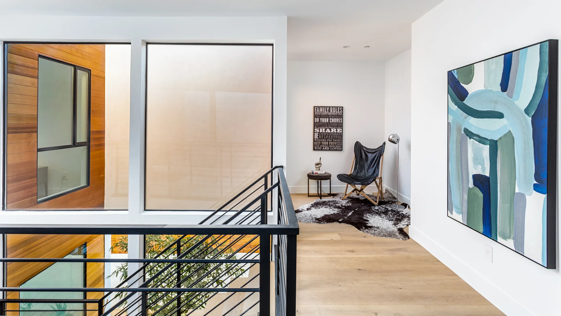 A modern hallway landing featuring a black leather butterfly chair on a cowhide rug beside a large blue abstract wall painting.