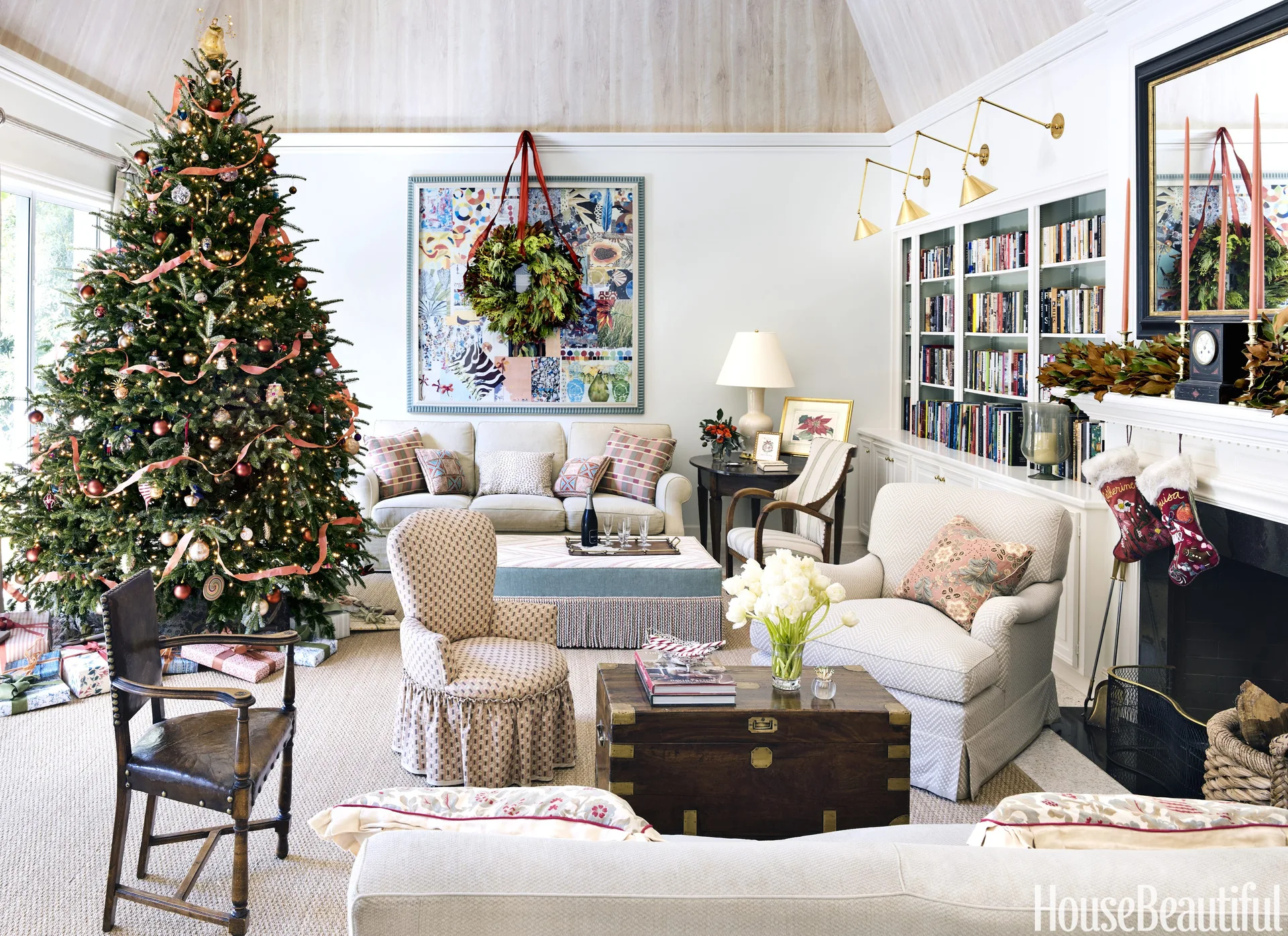 A festive living room features a decorated Christmas tree, patterned armchairs, and white built-in bookcases flanking a fireplace.