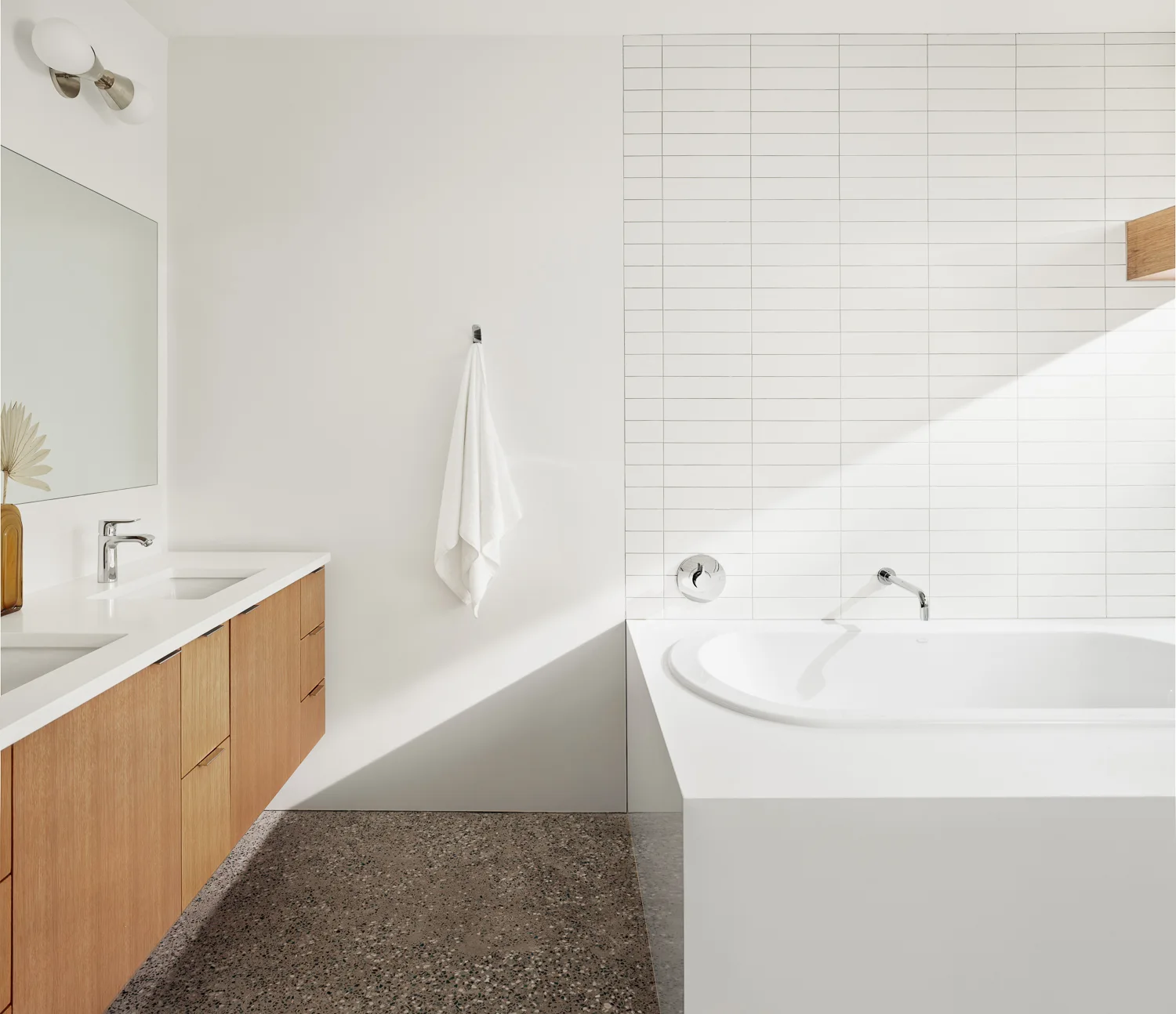A modern bathroom features a floating wood vanity next to a built-in white bathtub under a wall of stacked white subway tiles.