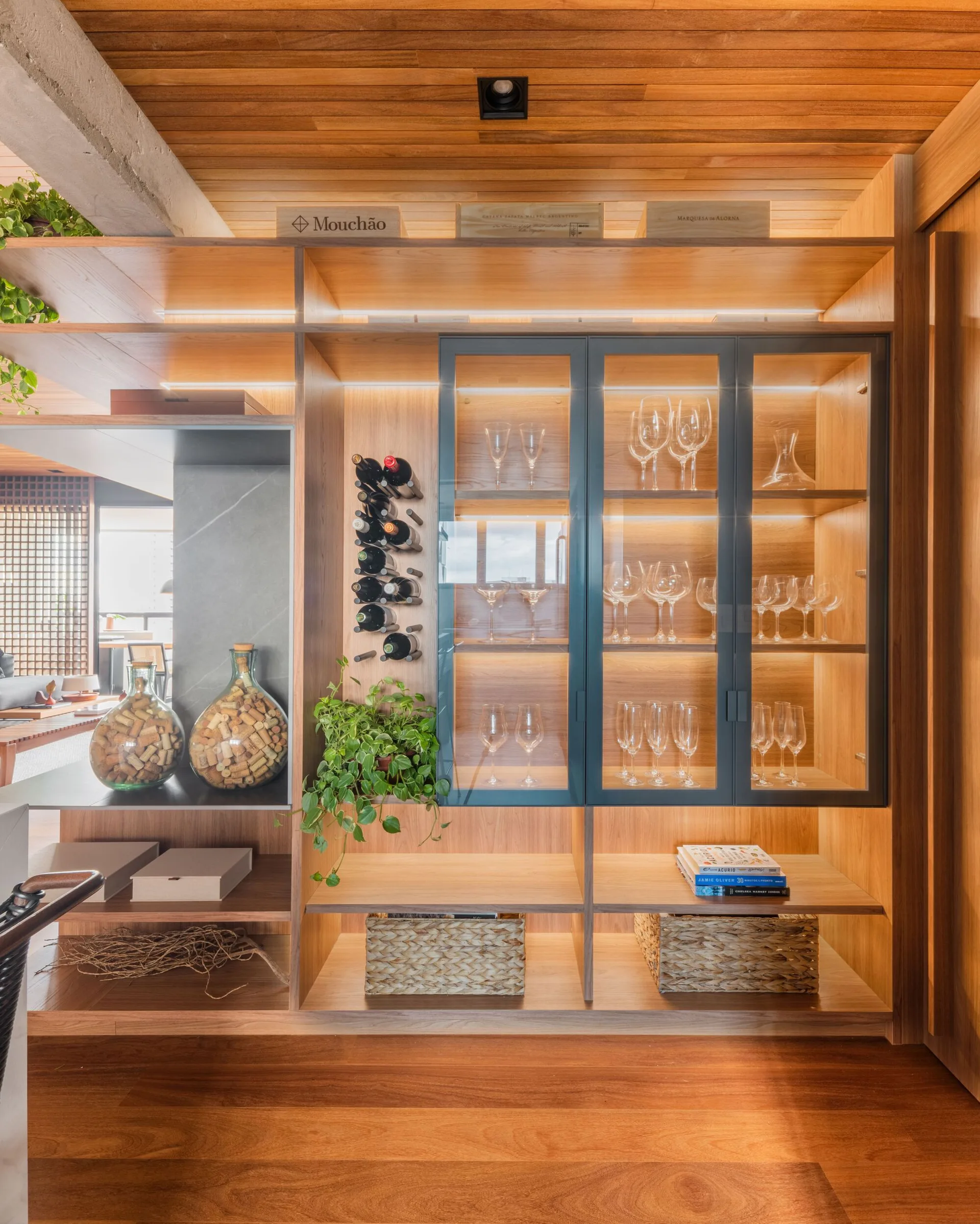 A built-in wooden wine cabinet features glass-door shelving for wine glasses, a metal bottle rack, and glowing integrated LED strip lighting.