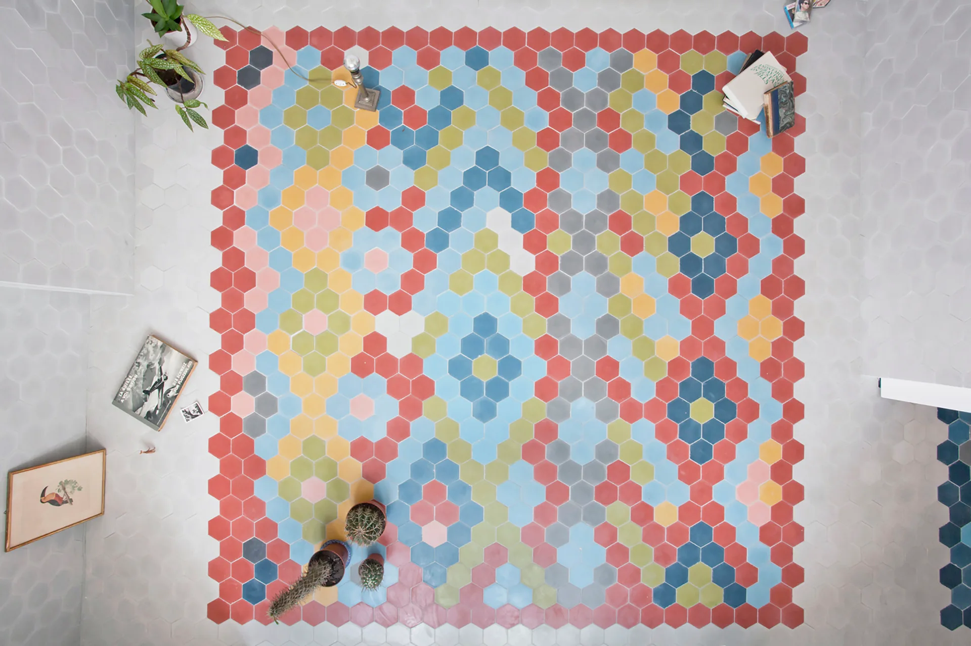 An overhead view of a floor featuring multicolored hexagonal tiles arranged in a bright geometric pattern surrounded by plain grey tiles.