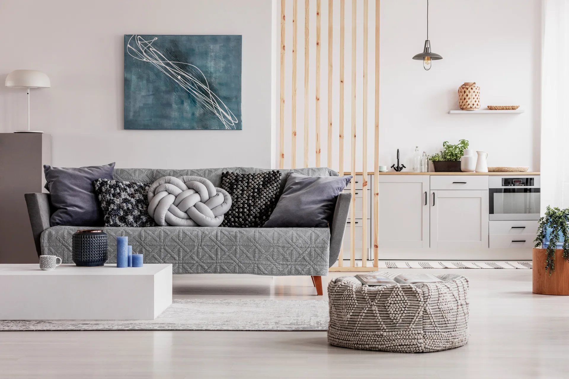 A grey quilted sofa sits in front of a light wood slatted room divider separating the living room from a light grey kitchen.