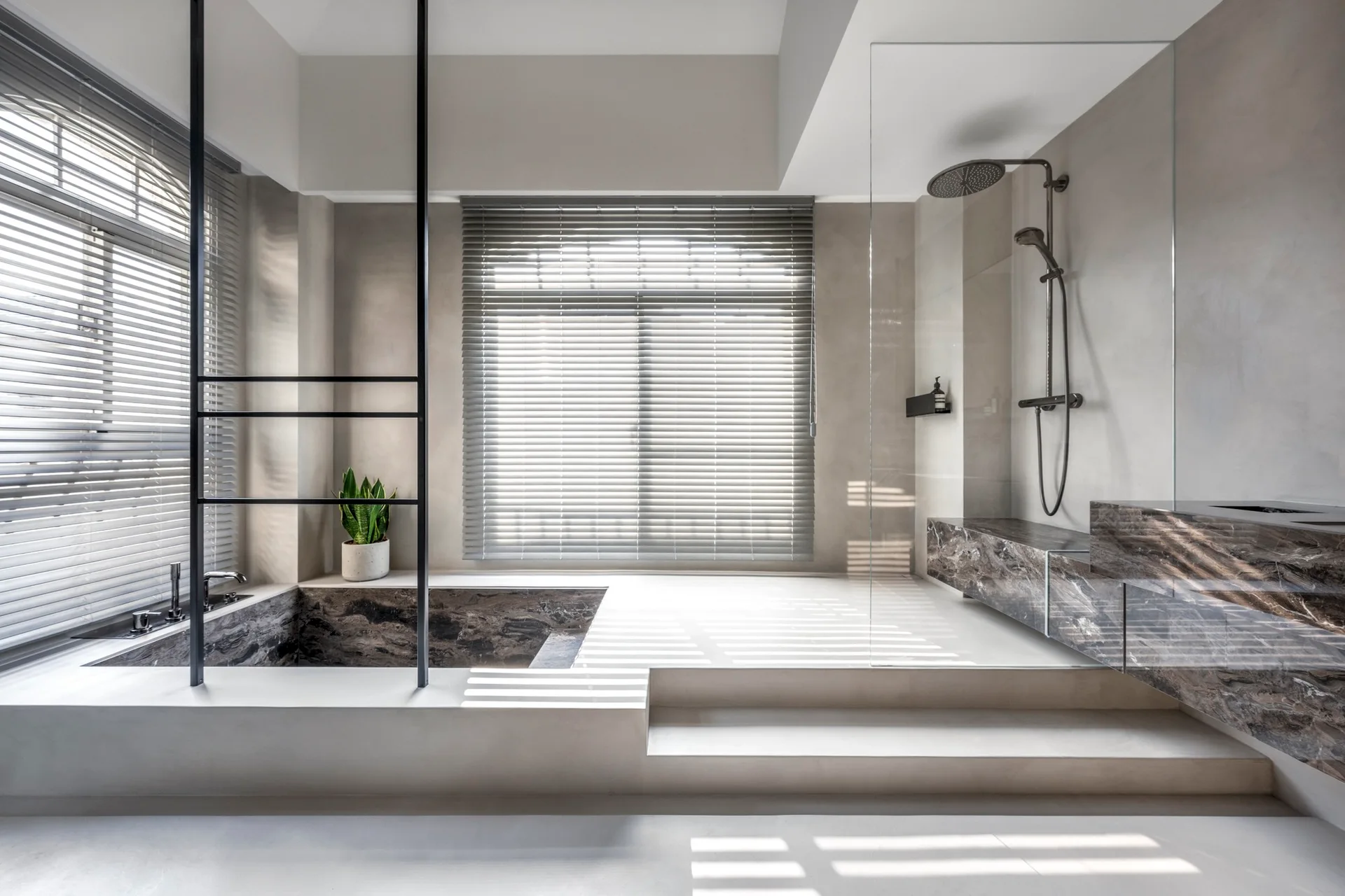 A minimalist grey bathroom featuring a sunken marble bathtub, a raised platform with a glass shower enclosure, and windows with grey horizontal blinds.