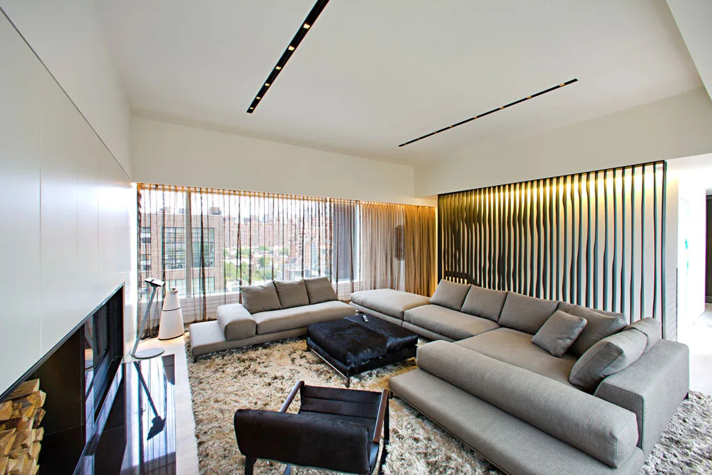 A modern living room features a large gray sectional sofa, a textured rug, and a vertical slatted accent wall with warm lighting.
