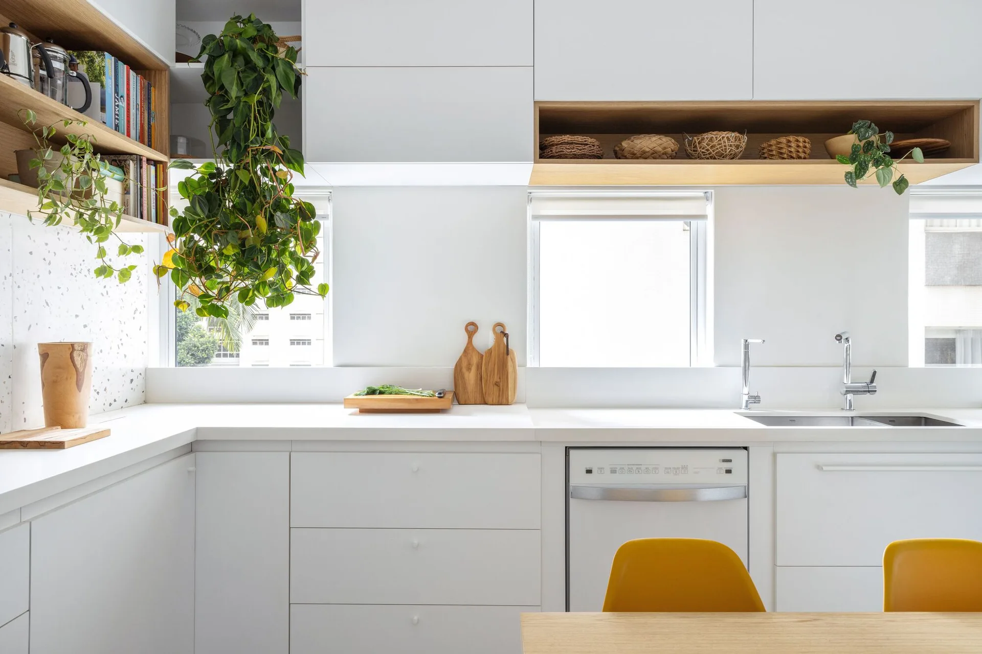 A bright modern kitchen featuring flat-panel white cabinetry, recessed wood shelving with items, and windows set between upper cabinets.