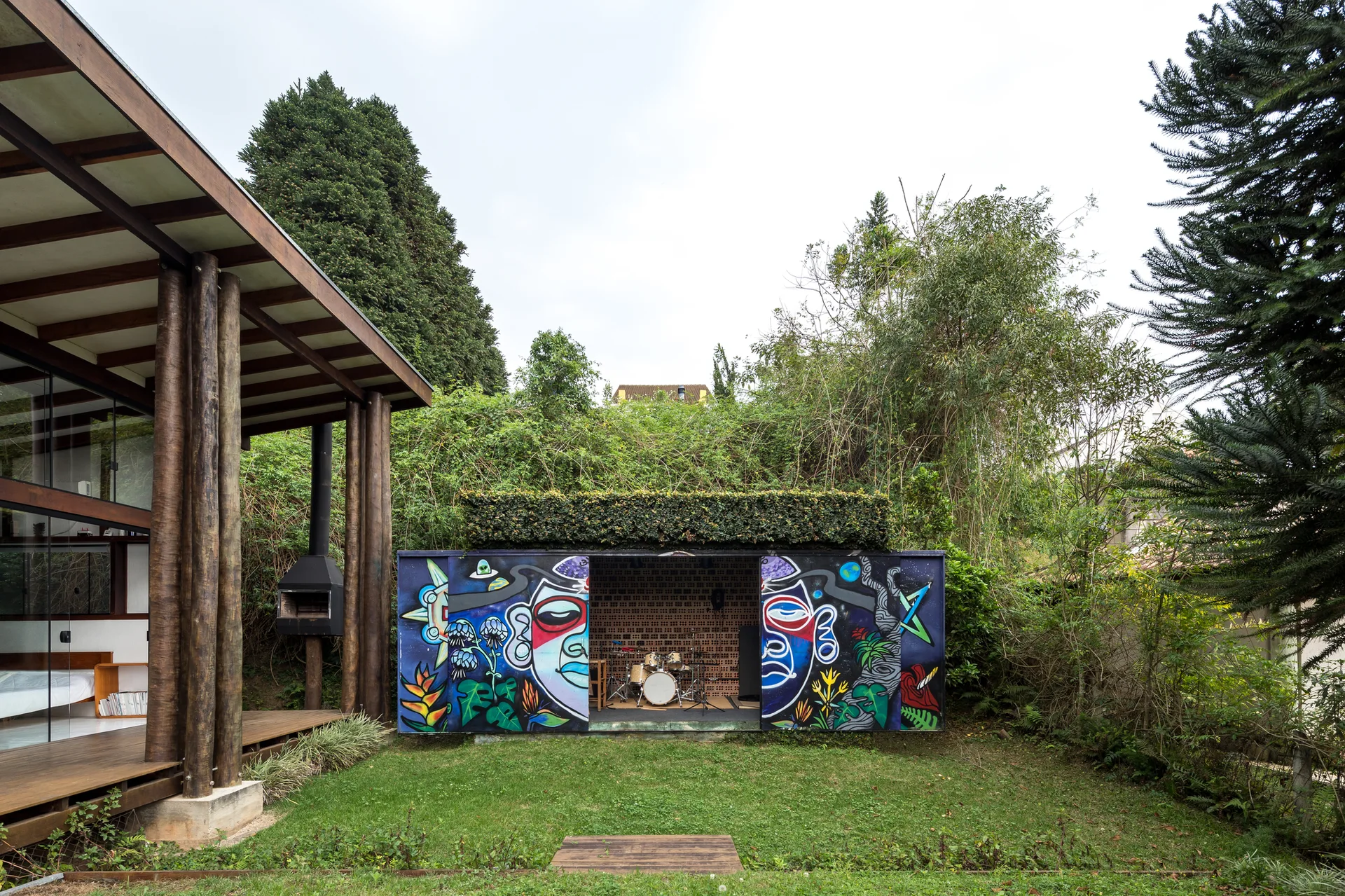 A backyard garden features a small music studio with a colorful painted mural on its open doors, a drum kit inside, and a living green roof.