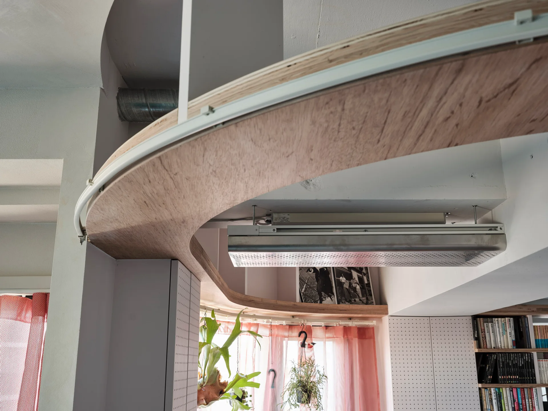 A curved plywood architectural soffit runs across a white ceiling above white pegboard wall panels and sheer red curtains.