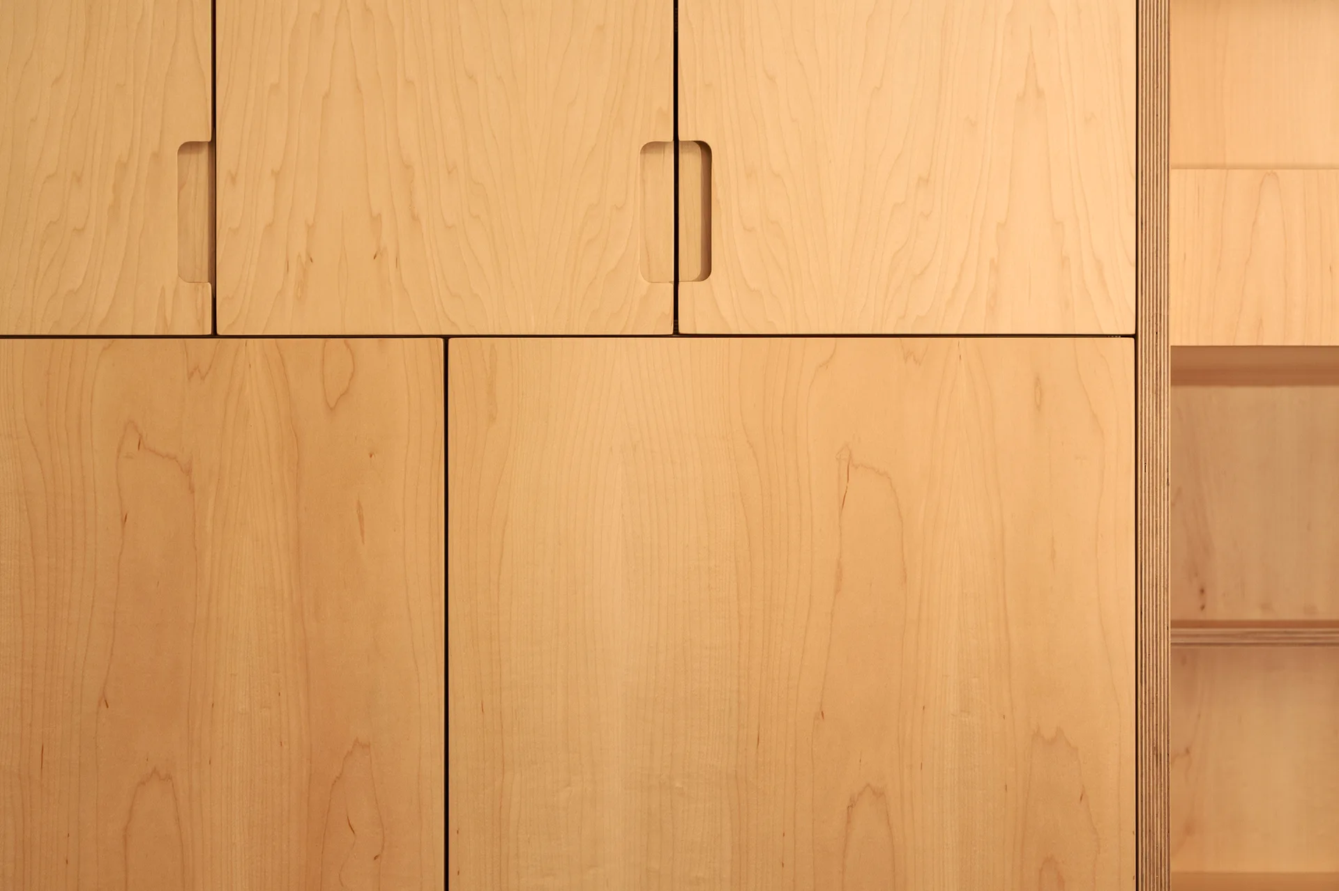 Close-up of light wood plywood cabinet doors with recessed oval cutouts as handles and an exposed layered edge detail on the side.