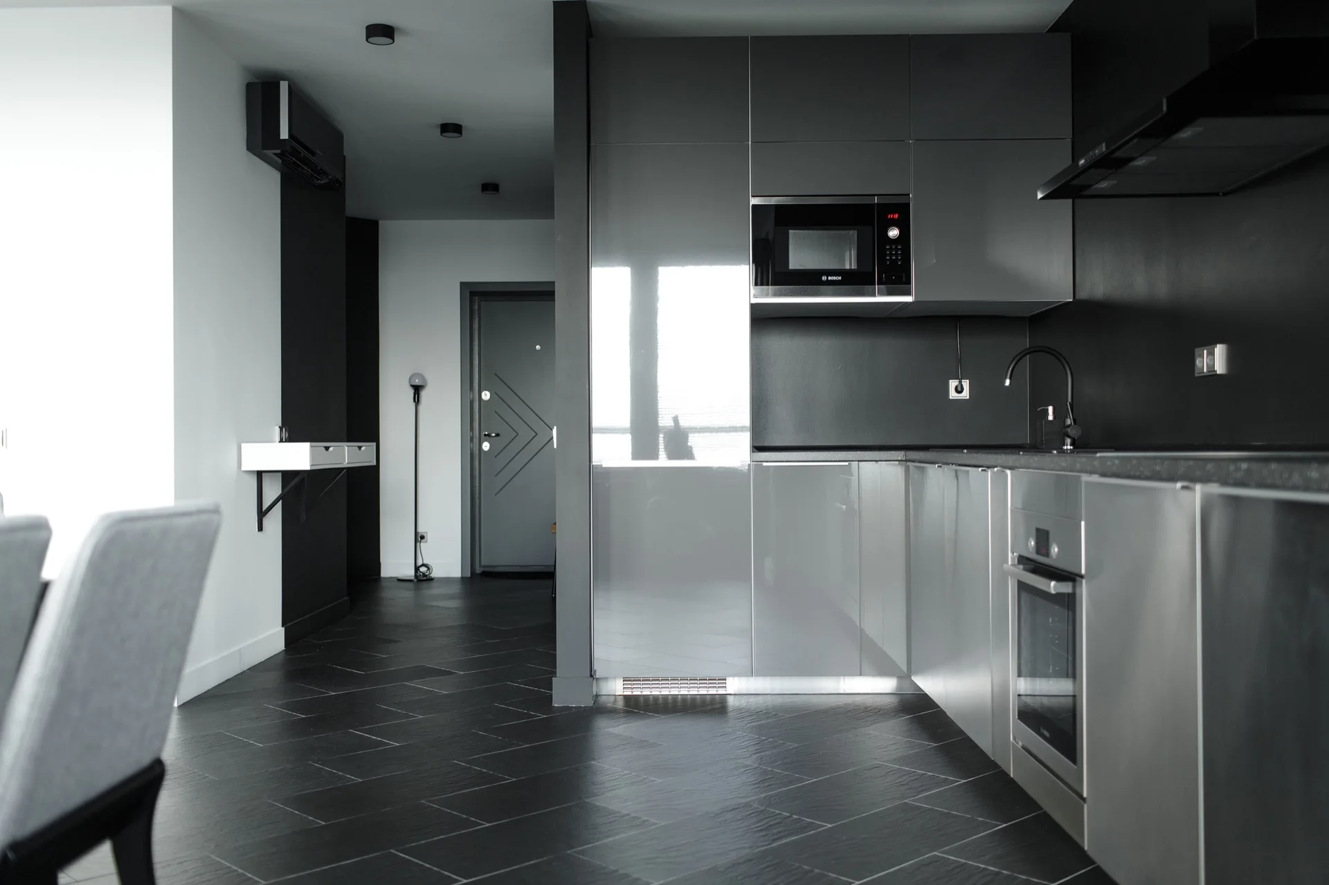 A minimalist kitchen featuring glossy grey cabinets, integrated stainless steel appliances, and a dark grey tiled floor laid in a herringbone pattern.