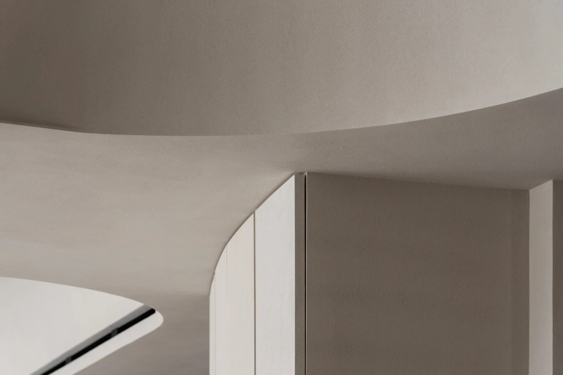 A close-up view of a minimalist curved plaster ceiling and a vertical partition wall finished in a uniform matte beige.