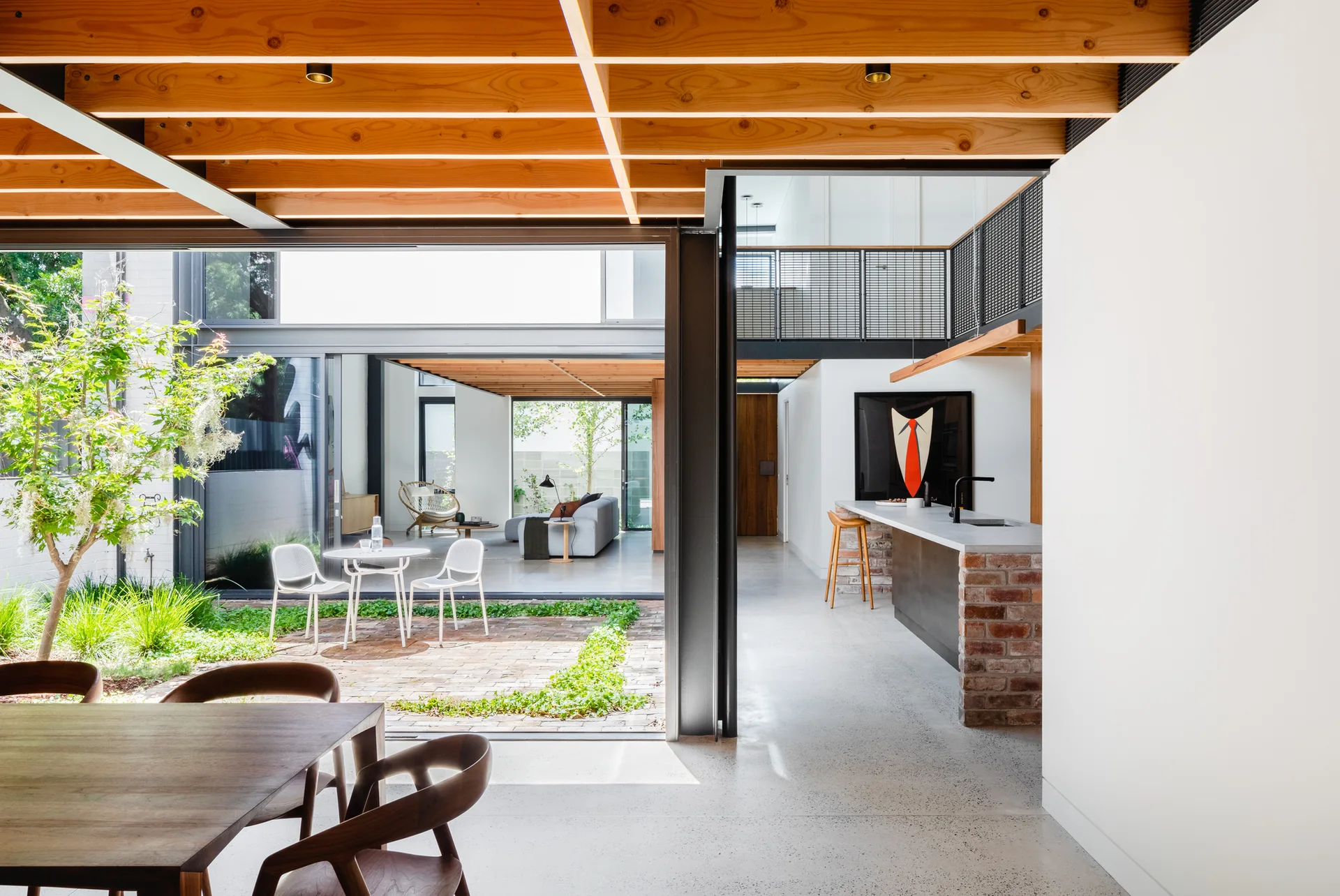 A modern open-plan kitchen and dining area with exposed wood ceiling beams, a brick island, and glass doors opening to a central courtyard garden.