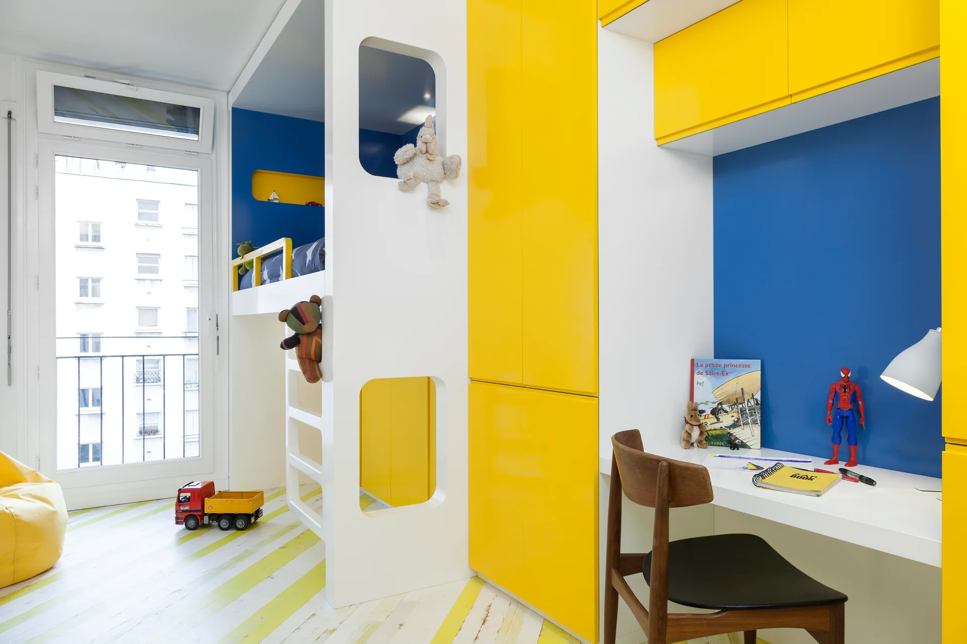 A modern kids' bedroom featuring a white and yellow built-in bunk bed unit, an integrated study desk, and diagonal yellow and white floor stripes.