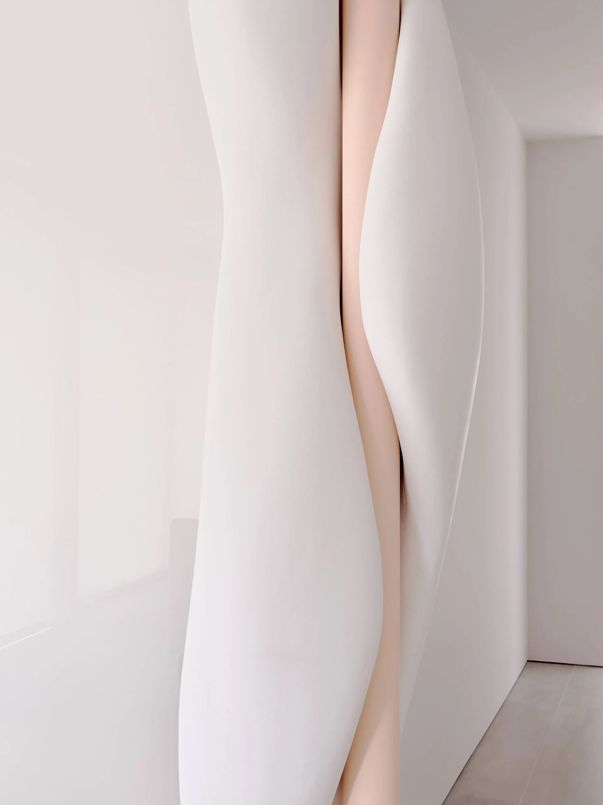 A smooth, sculptural white wall feature curves gently to reveal a soft blush pink recessed vertical stripe in a minimalist interior.
