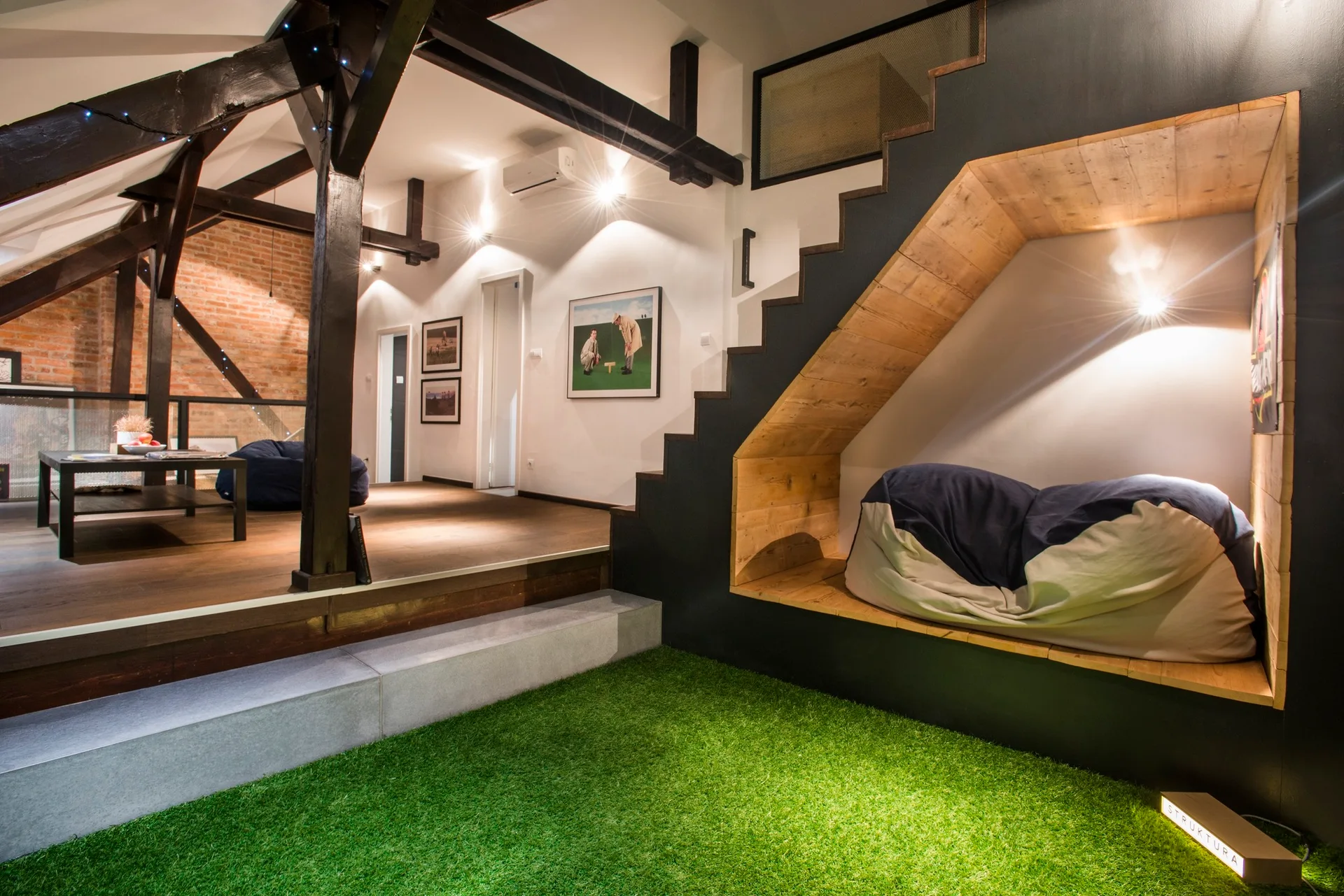 A modern split-level living space with a green artificial turf floor, a black staircase with a wood-lined nook, and a raised wooden platform.
