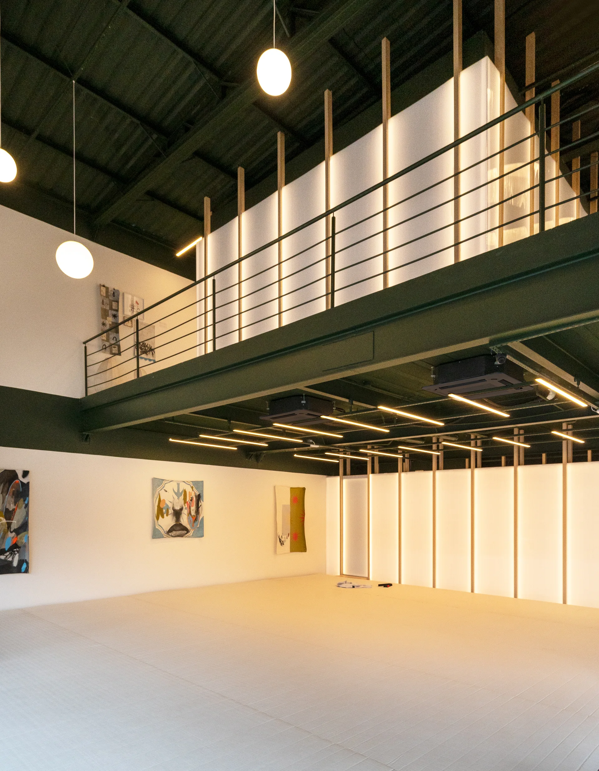 A spacious training studio features a large off-white floor mat, an elevated mezzanine with a backlit wooden screen, and hanging globe lights.