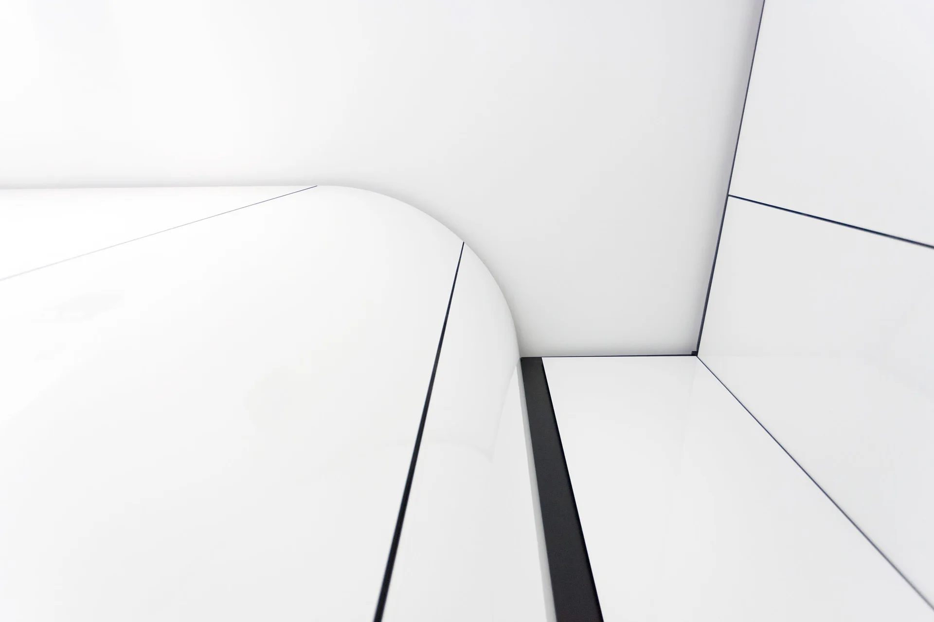A close-up of glossy white architectural wall panels featuring a curved corner design with thin dark seams.