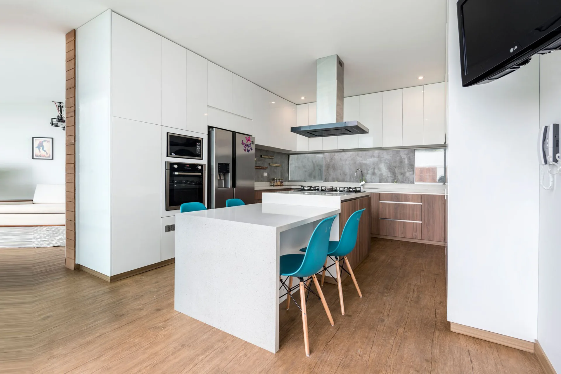 A modern kitchen with two-tone cabinetry, a white waterfall island, vibrant blue chairs, and stainless steel appliances.