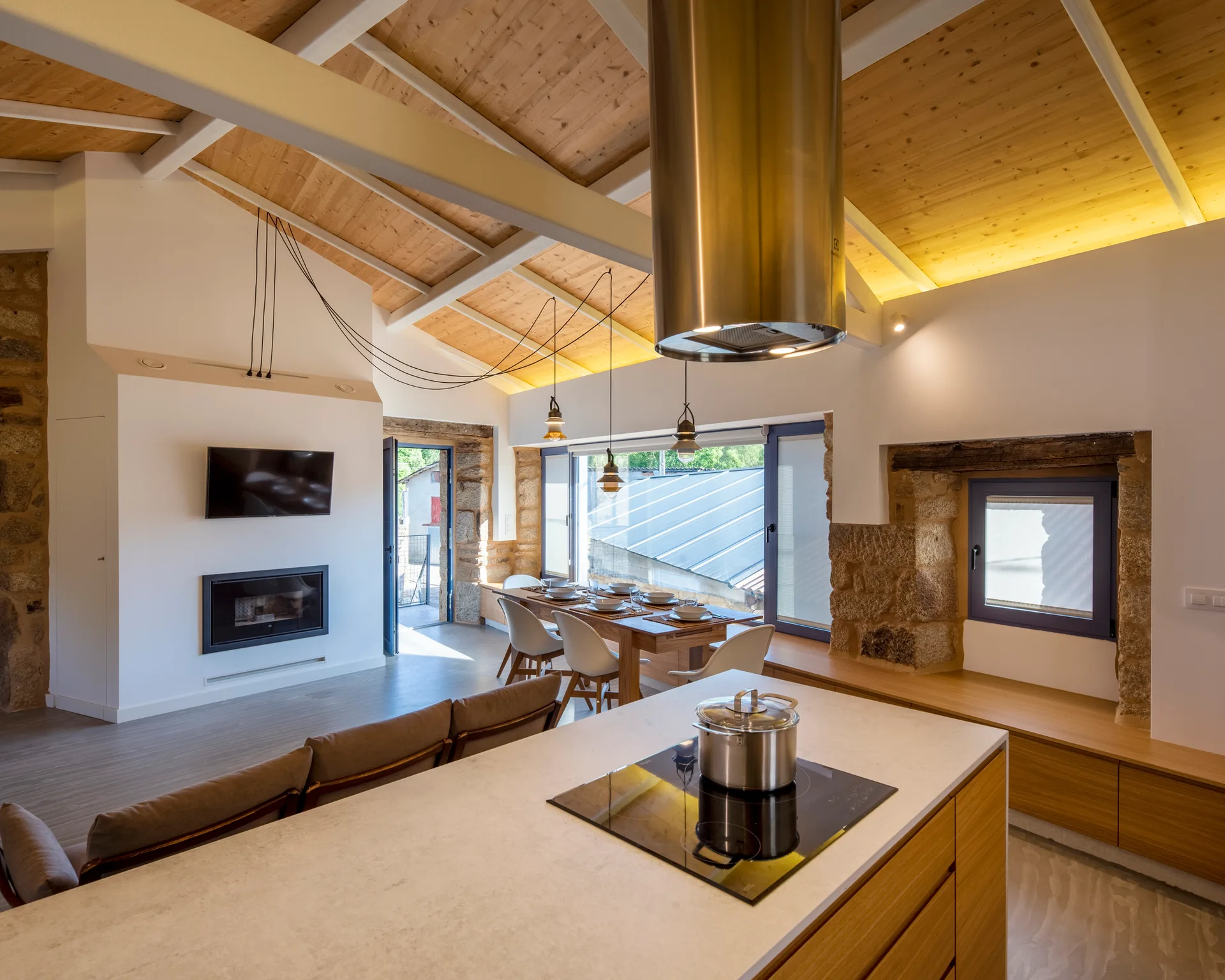 An open plan kitchen and dining area features a vaulted wood ceiling, white walls, stone masonry windows, and a large wood kitchen island.