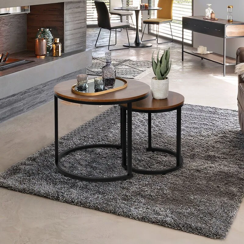 Two round nesting coffee tables with wood tops and black metal legs sit on a shaggy grey area rug in front of a modern fireplace.