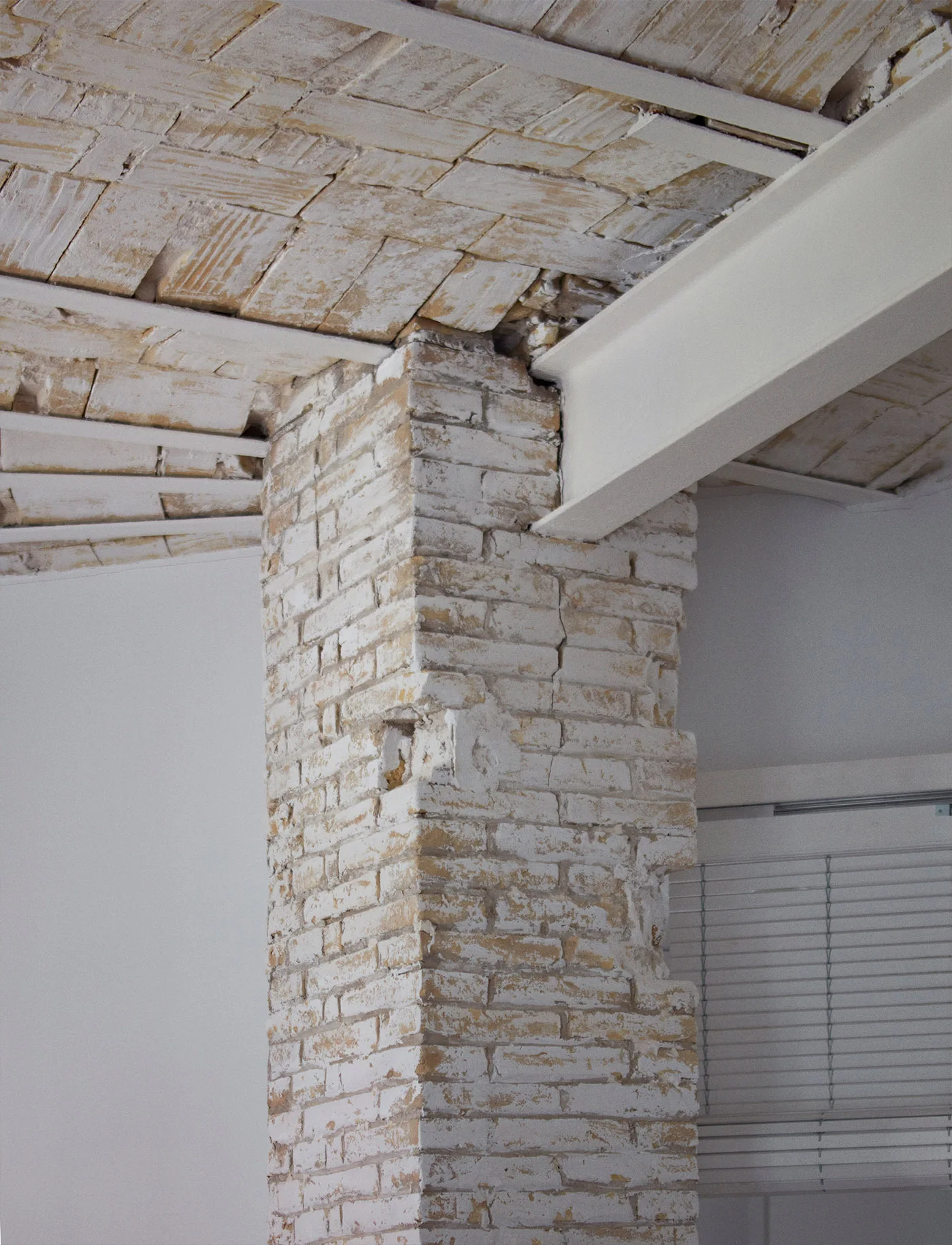 A close-up of an interior architectural detail featuring an exposed whitewashed brick column and ceiling paired with a painted white steel I-beam.
