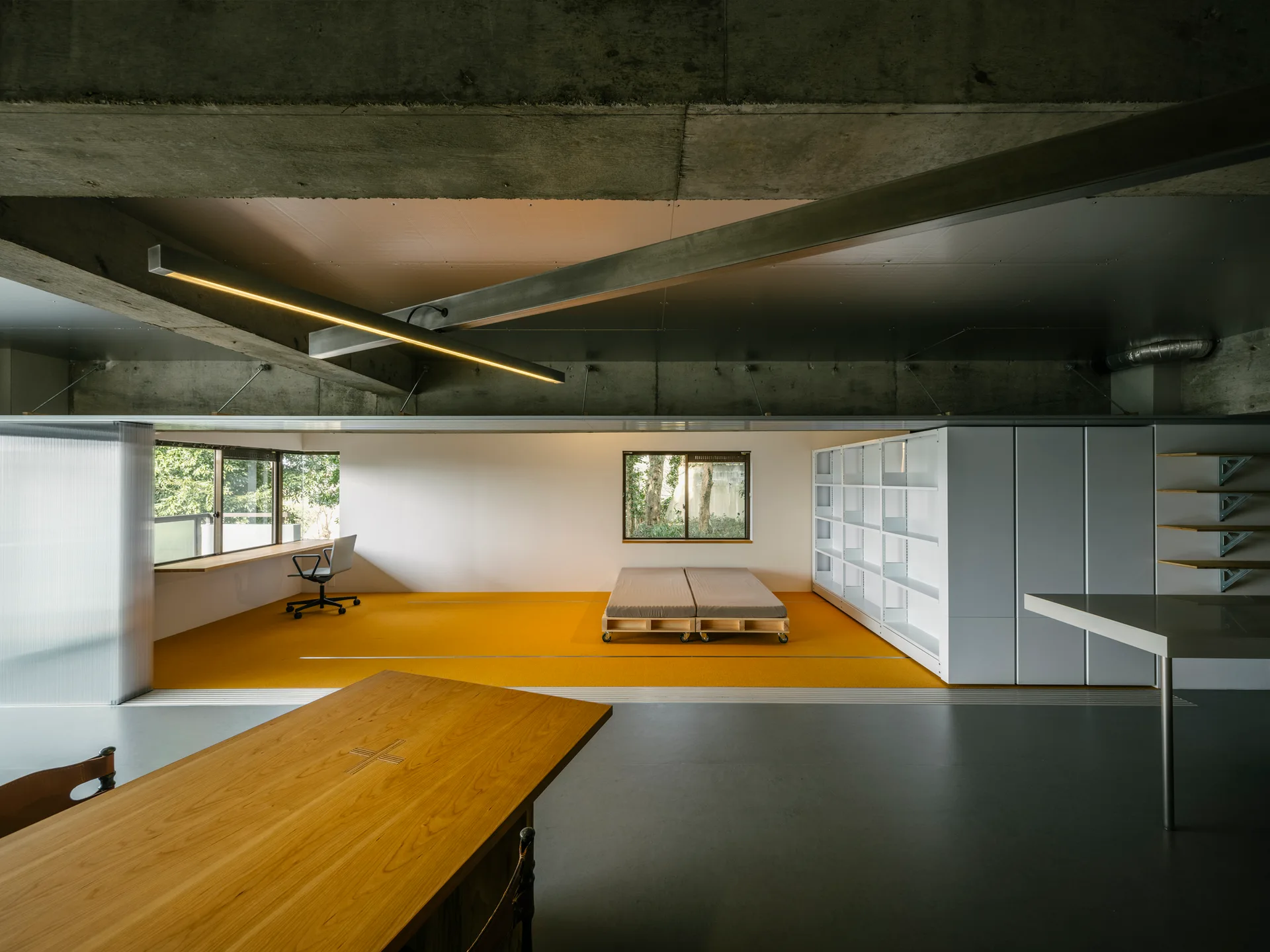 A minimalist loft interior featuring a bright yellow carpeted zone, an exposed concrete ceiling, and white modular storage units.