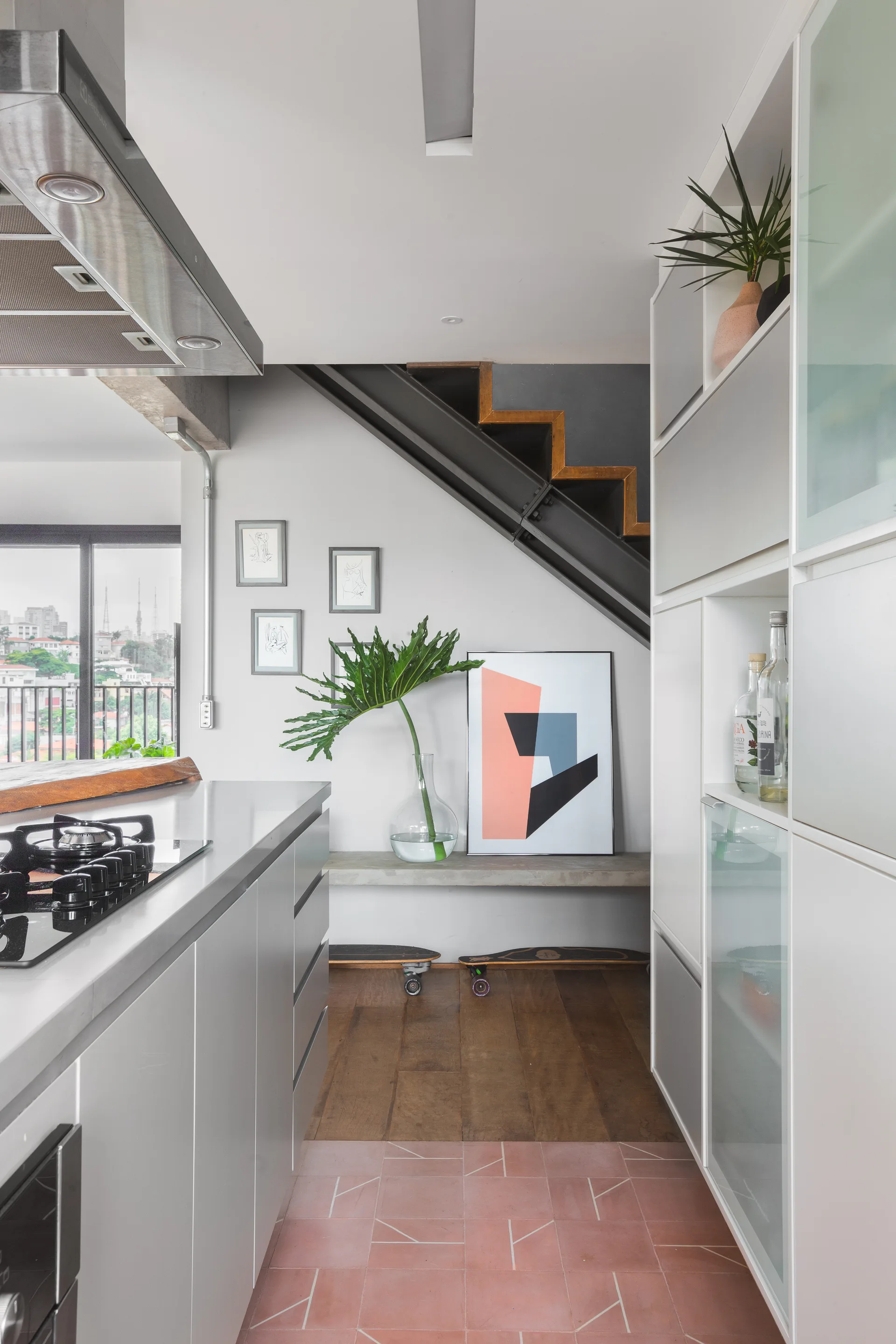 A modern kitchen features a grey island with a gas cooktop, white modular cabinets, and an industrial steel staircase with a concrete bench underneath.