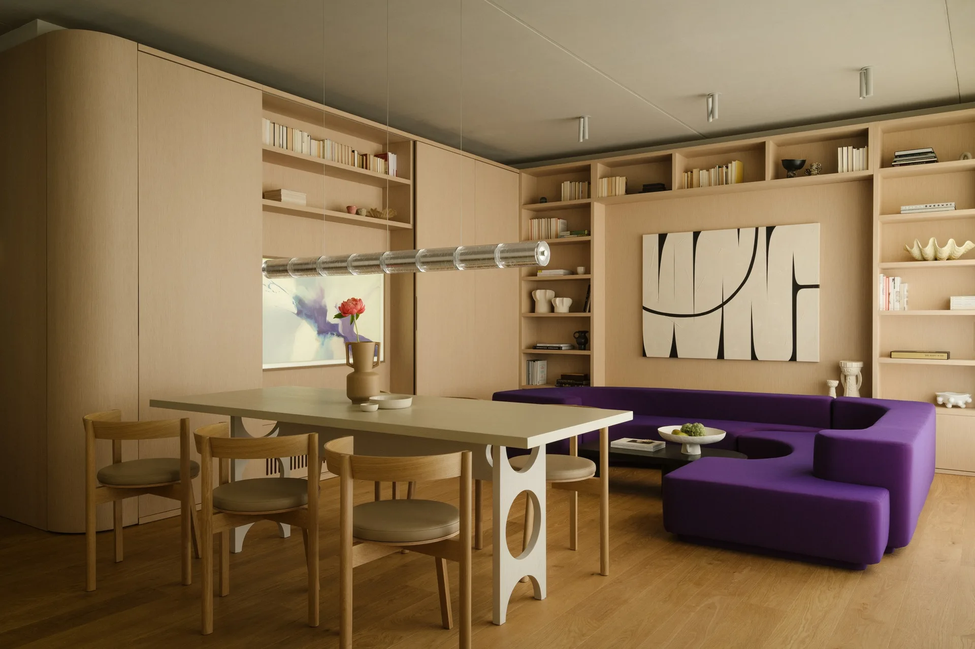 A contemporary open-plan dining space featuring light oak cabinetry, a white dining table with rounded chairs, and a deep purple sofa in the background.