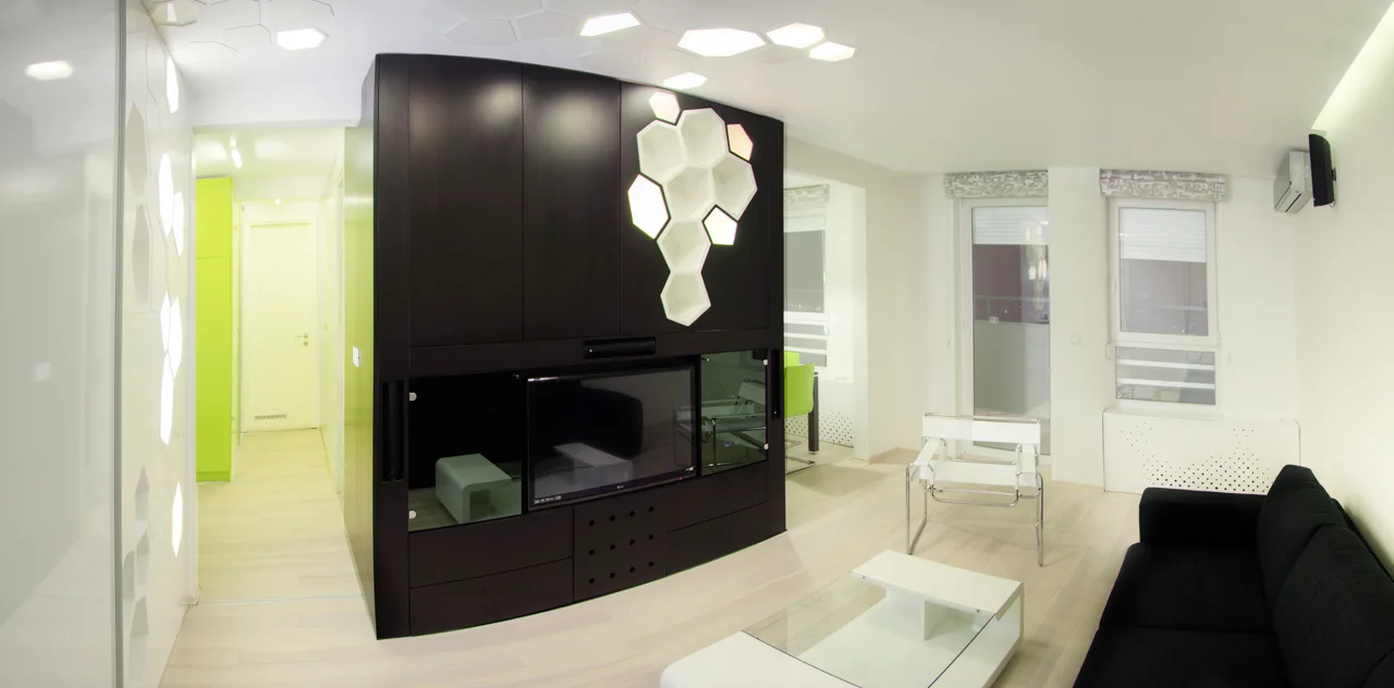 A modern living room features a dark central partition cabinet with backlit hexagonal shelves, a black sofa, and minimalist white furniture.