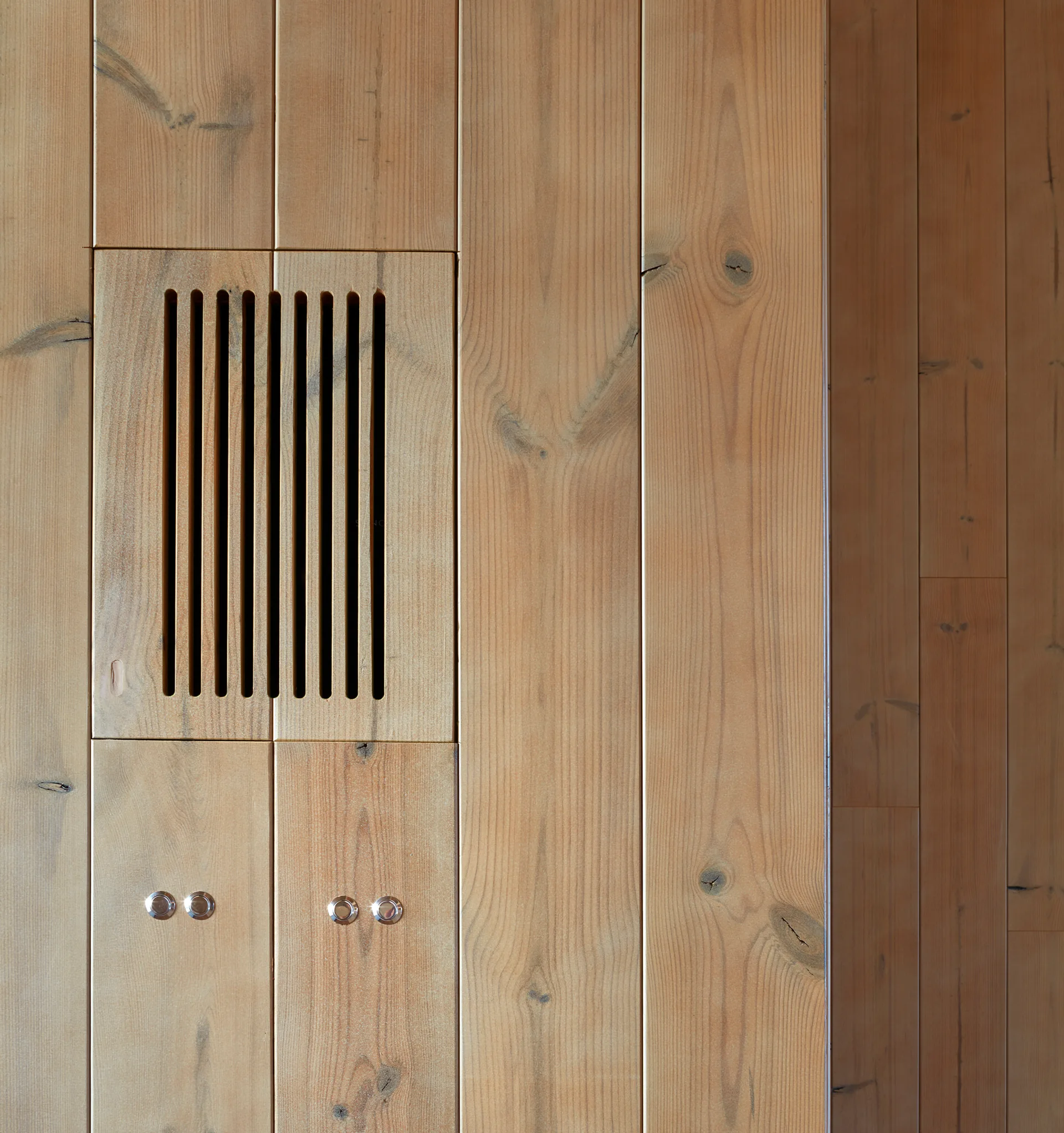 A close-up of light brown vertical wood paneling featuring an integrated wooden slotted air vent and four small circular metal control buttons.