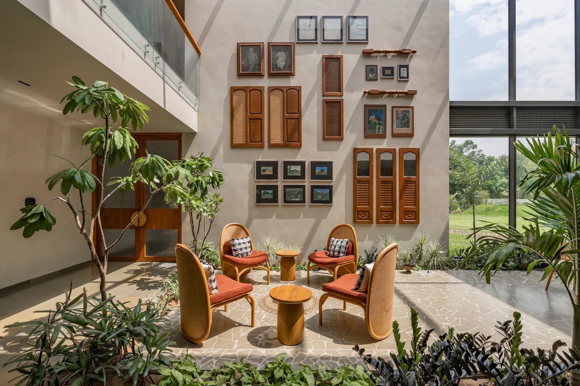Four terracotta cane armchairs are arranged around low wooden tables on a flagstone floor in a sunlit indoor courtyard.