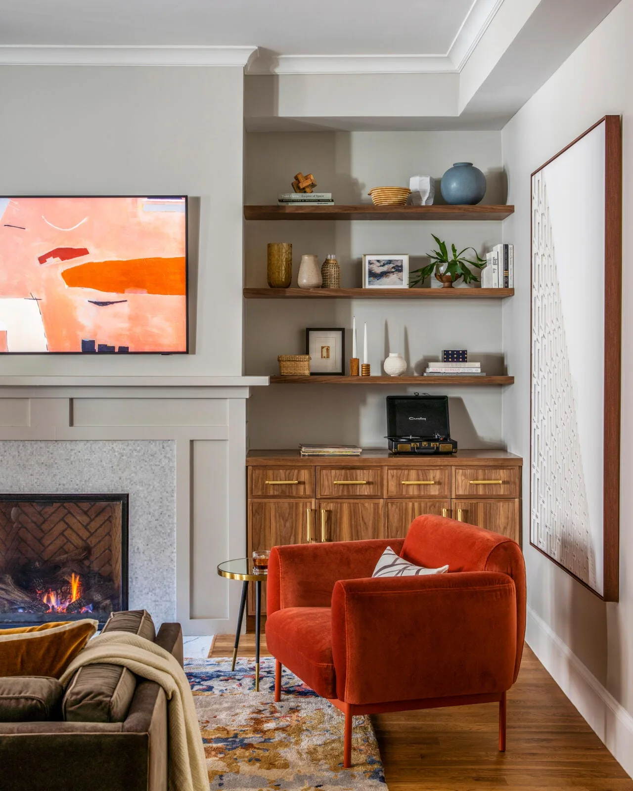 A living room corner features wood floating shelves over a built-in cabinet, next to a tiled fireplace and a plush orange armchair.