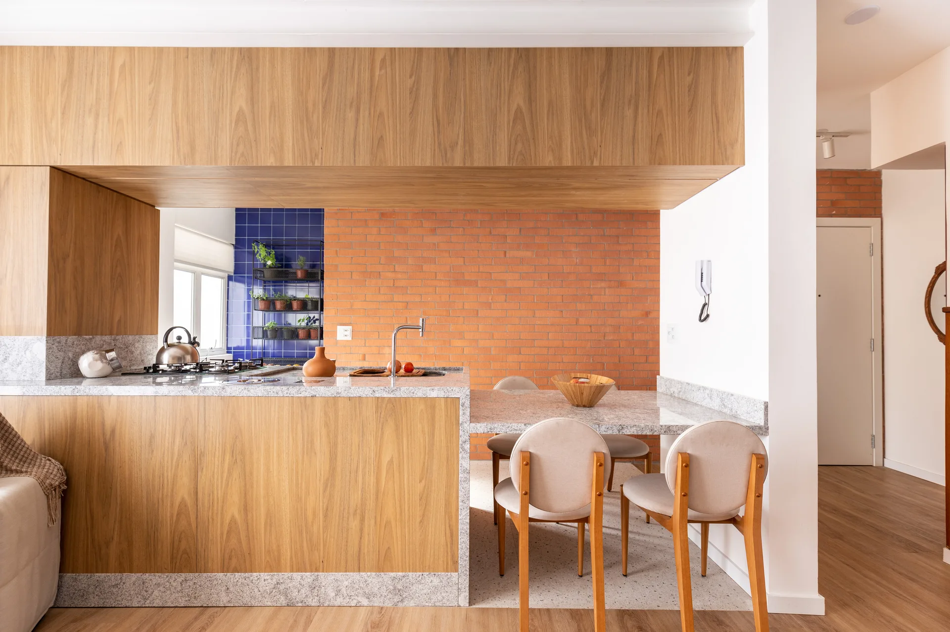 A modern kitchen features a wood-paneled island with a speckled stone countertop, an exposed red brick wall, and a blue tile backsplash.
