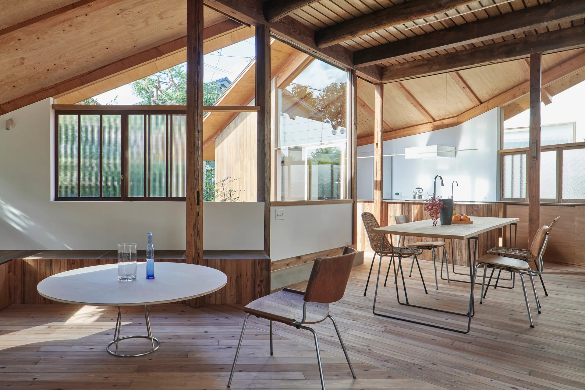 An airy interior features a vaulted wood ceiling with exposed timber beams, a low round coffee table, and a wooden dining table with chairs.