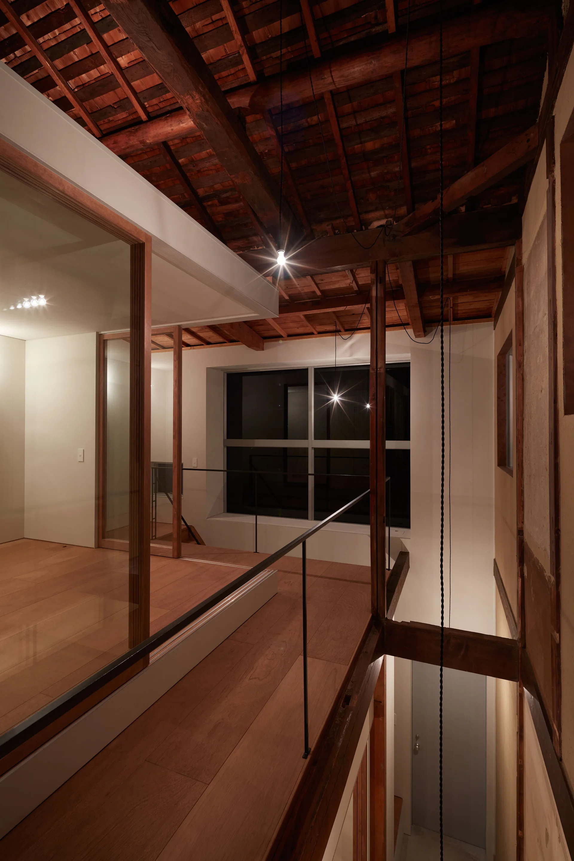 A modern wood mezzanine landing with a black metal railing and glass walls beneath an exposed dark timber ceiling structure.