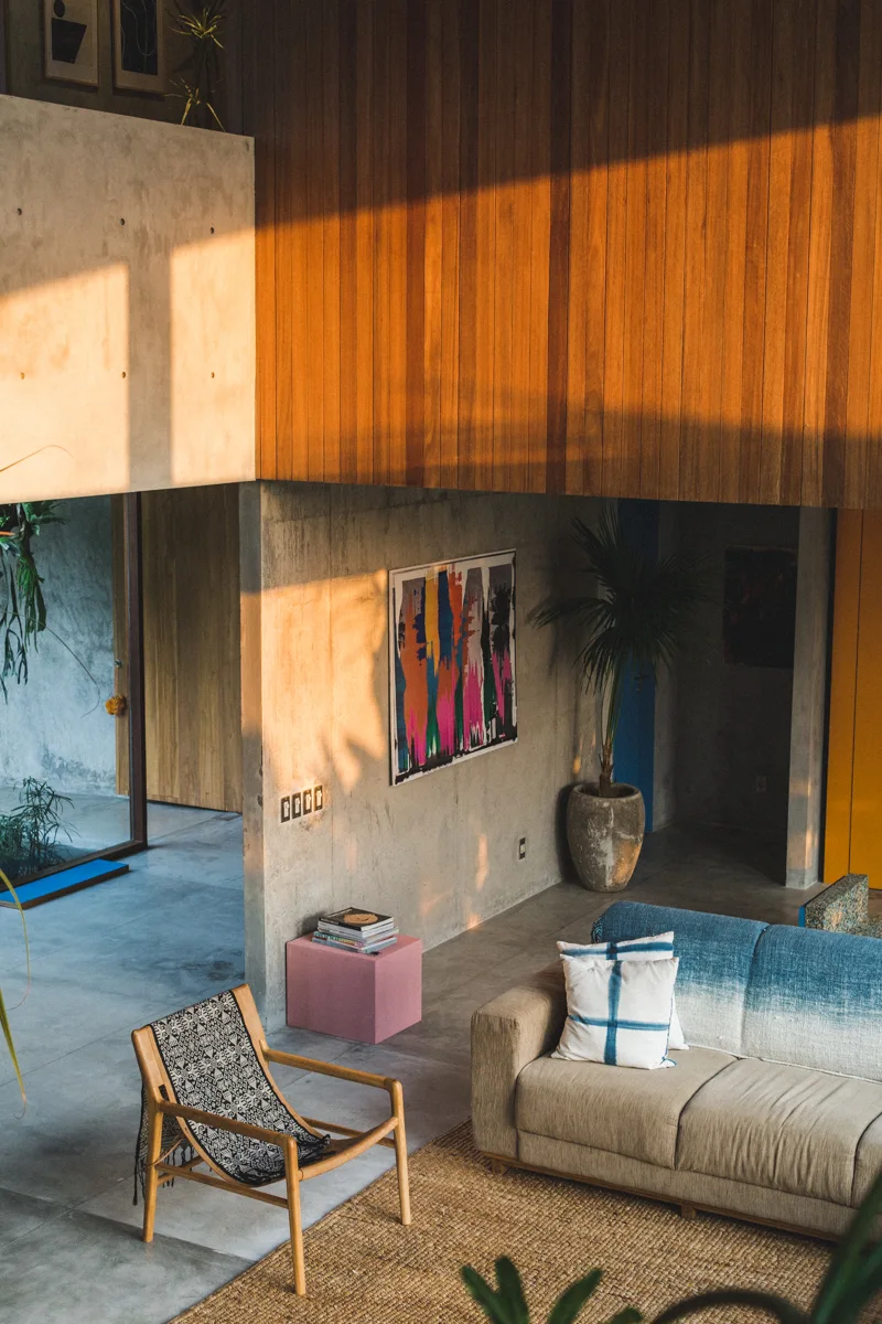 A modern living room features a blue gradient sofa, a wooden armchair on a jute rug, concrete walls, and a high wood-paneled upper wall.