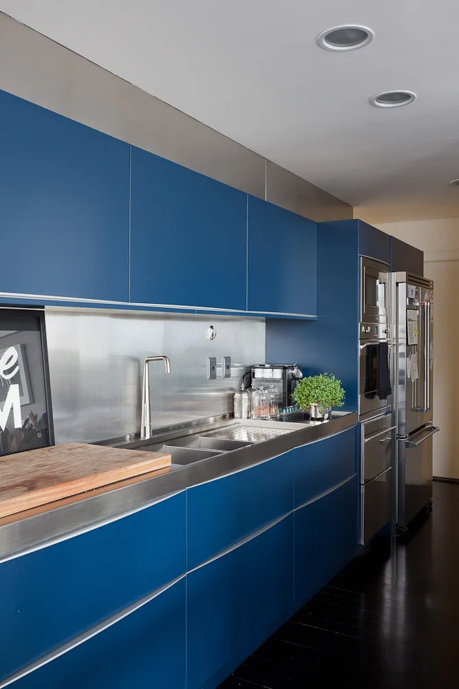 Modern kitchen featuring matte blue flat-front cabinetry, a stainless steel backsplash and countertop, and integrated appliances.